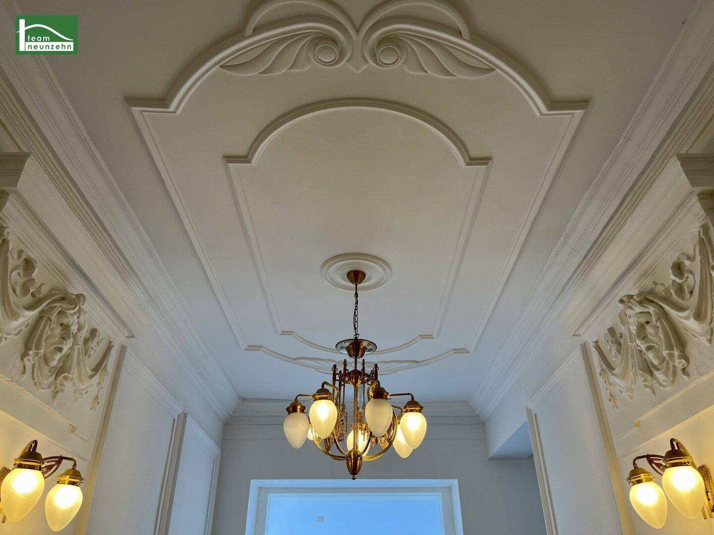 Prächtige Stuckdecke mit aufwendigen Verzierungen und einem eleganten Kronleuchter im klassischen Stil.