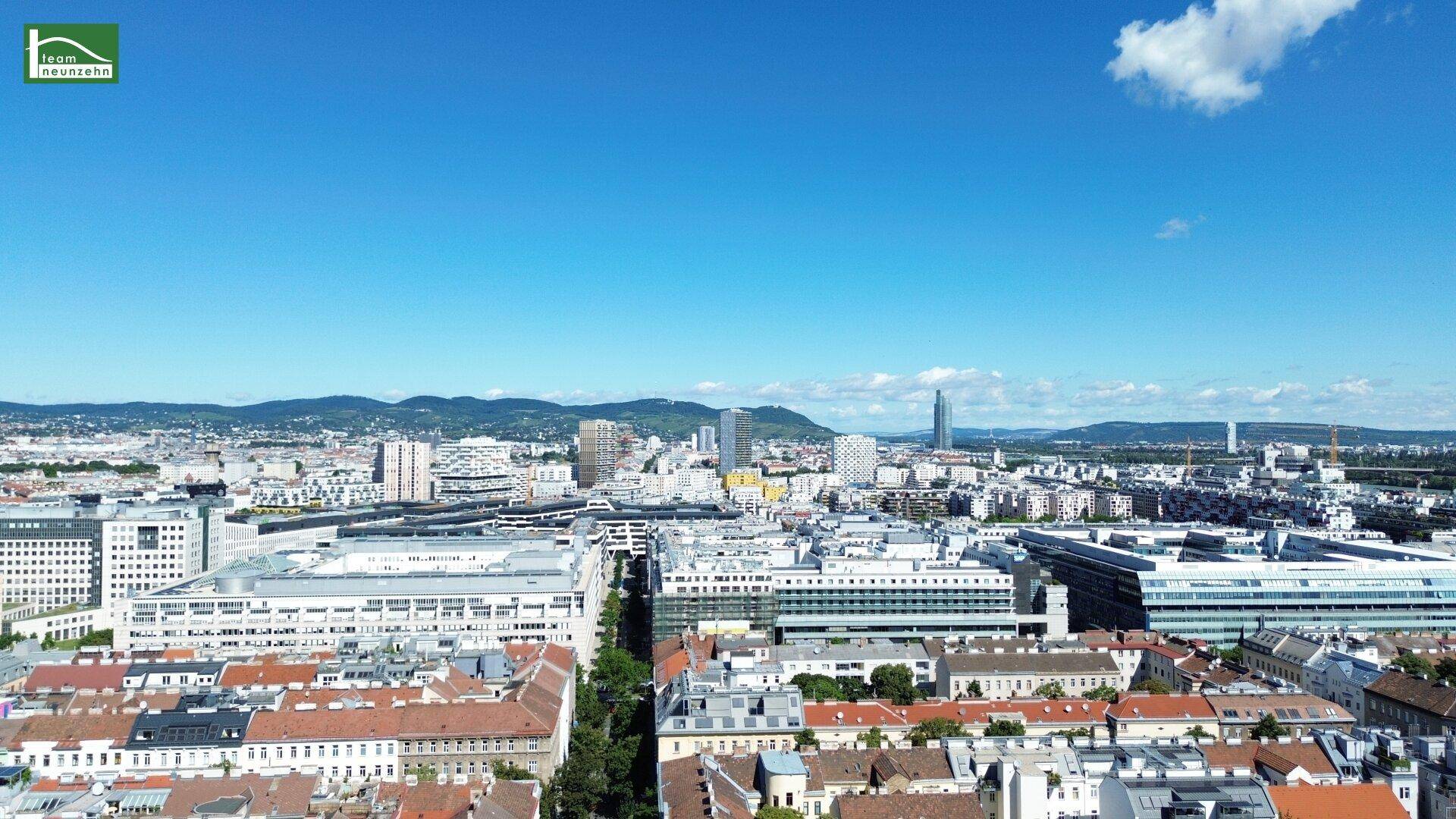 Weitläufiger Blick über die Stadt Wien mit vielen Gebäuden und Bergen im Hintergrund.
