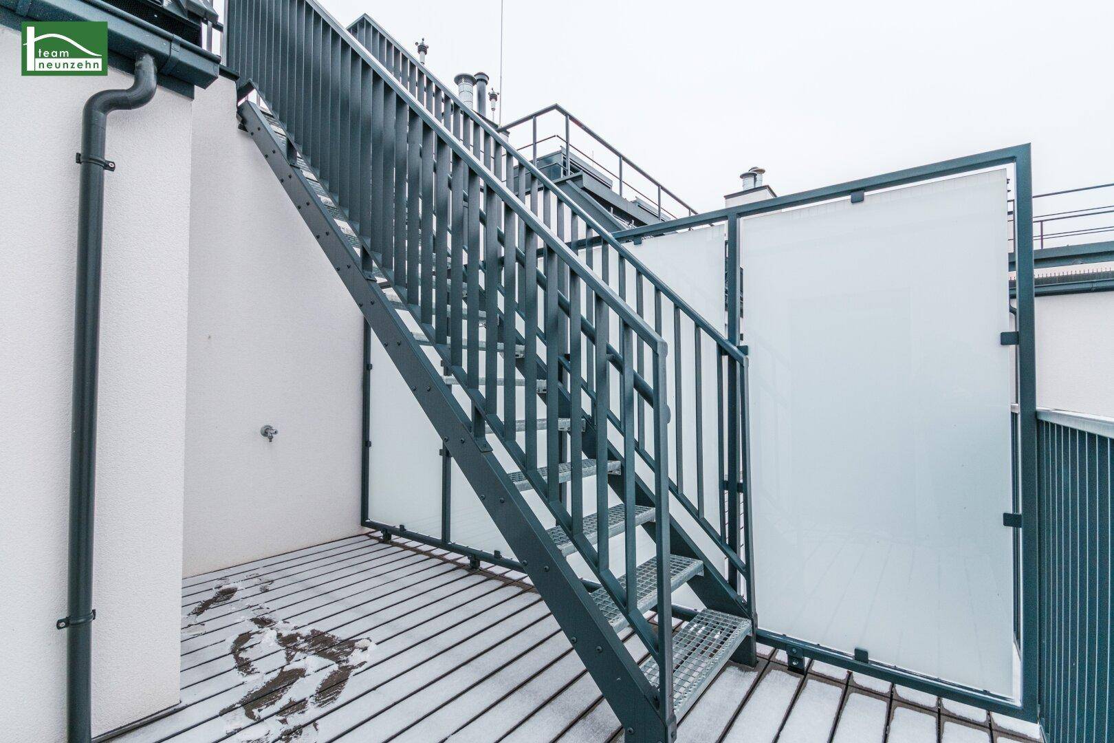 Metalltreppe führt zur oberen Dachterrasse mit Blick über die Dächer der Stadt.