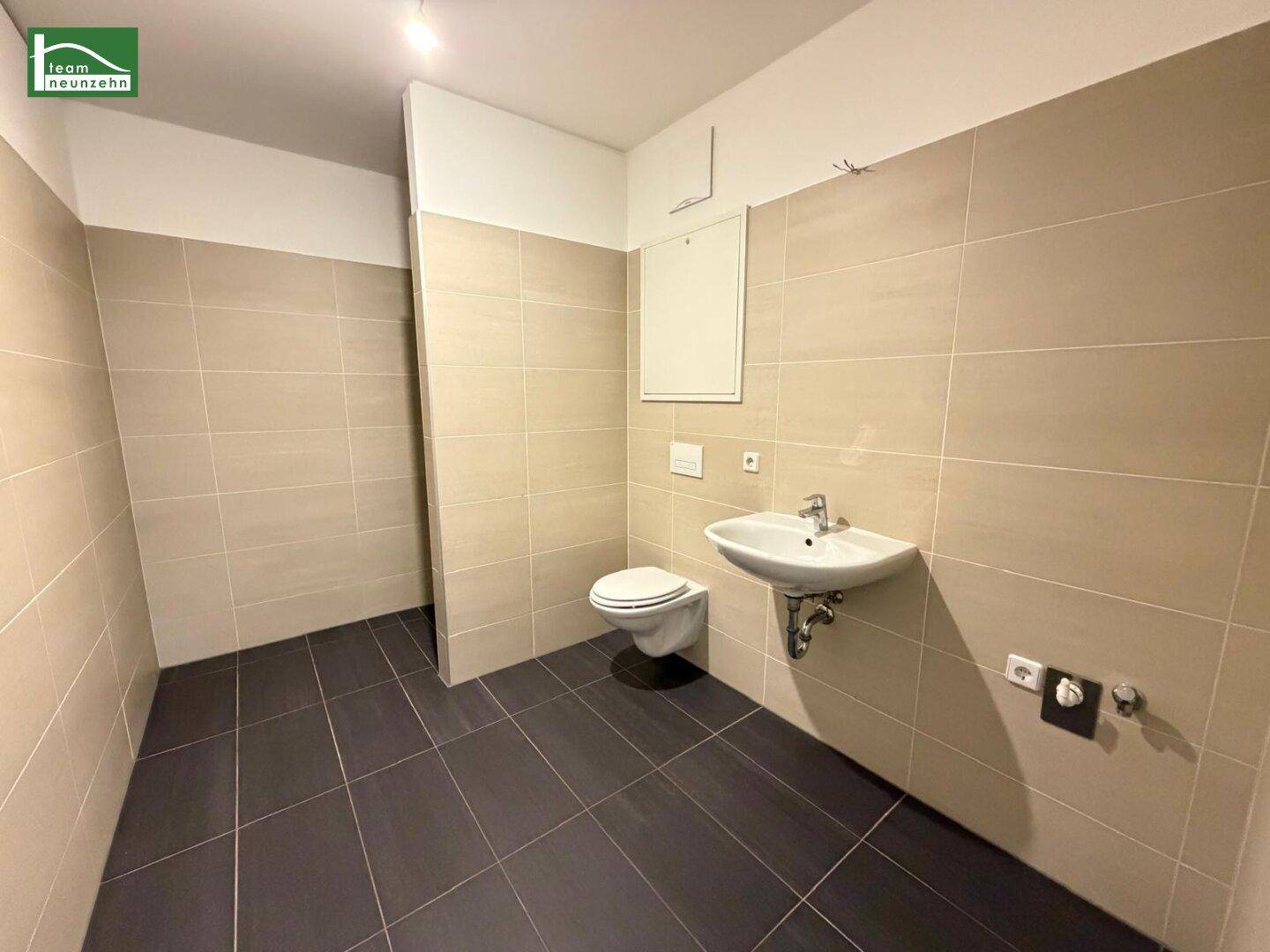 Modernes Badezimmer mit beigen und dunkelgrauen Fliesen, wandhängendem WC und Waschbecken.