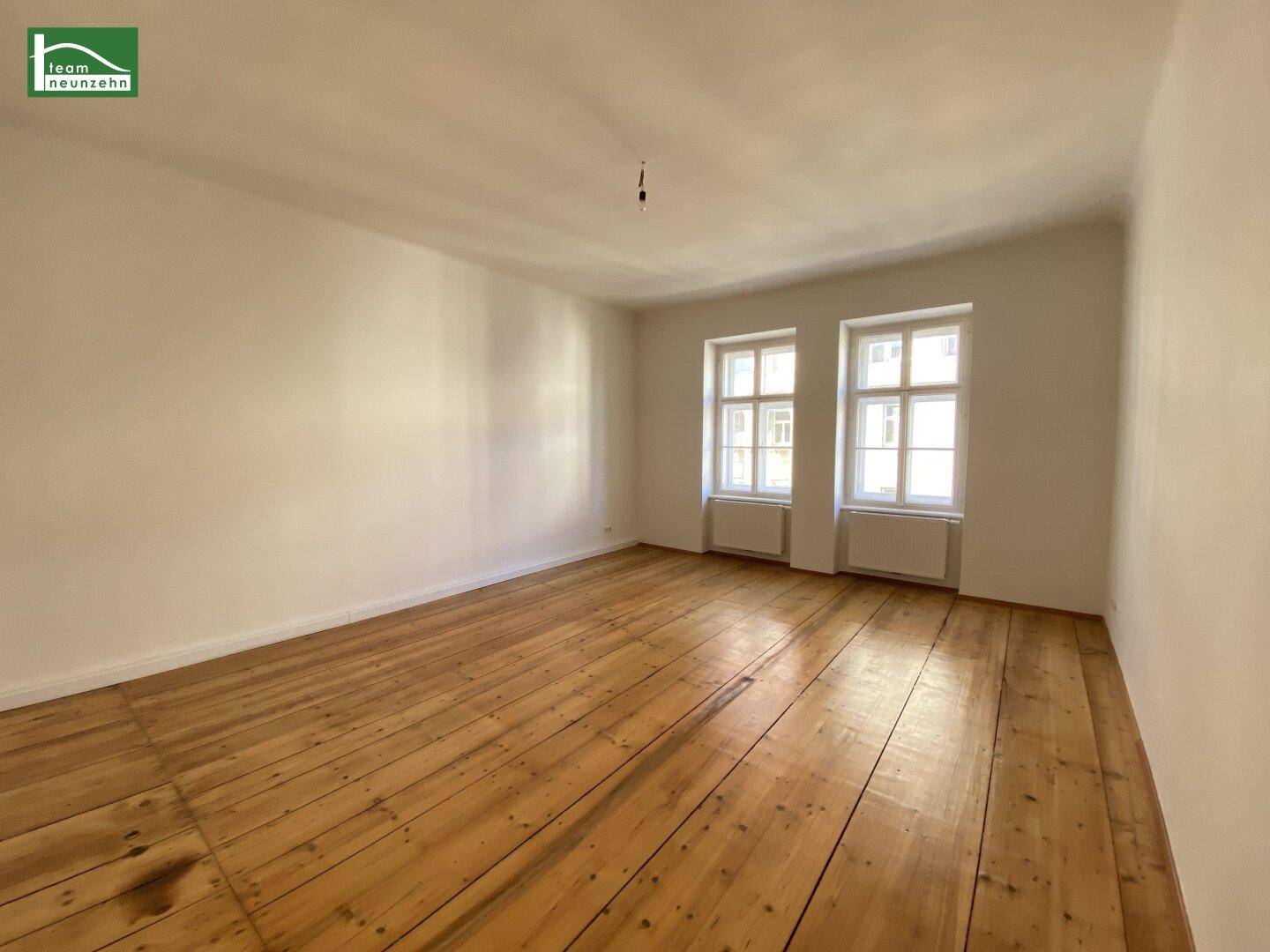Helles, leeres Zimmer mit Holzdielenboden und zwei Fenstern, bereit zur individuellen Gestaltung.