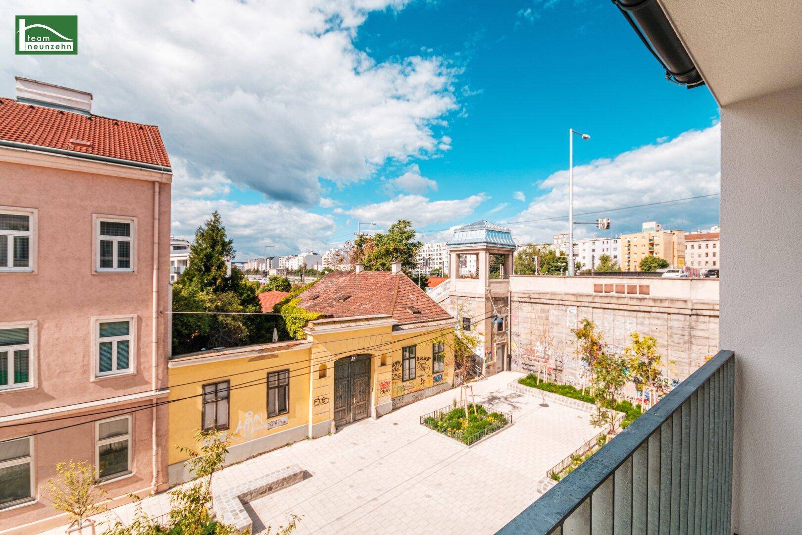 Blick vom Balkon auf einen charmanten Innenhof mit alten Gebäuden und Stadtpanorama im Hintergrund.