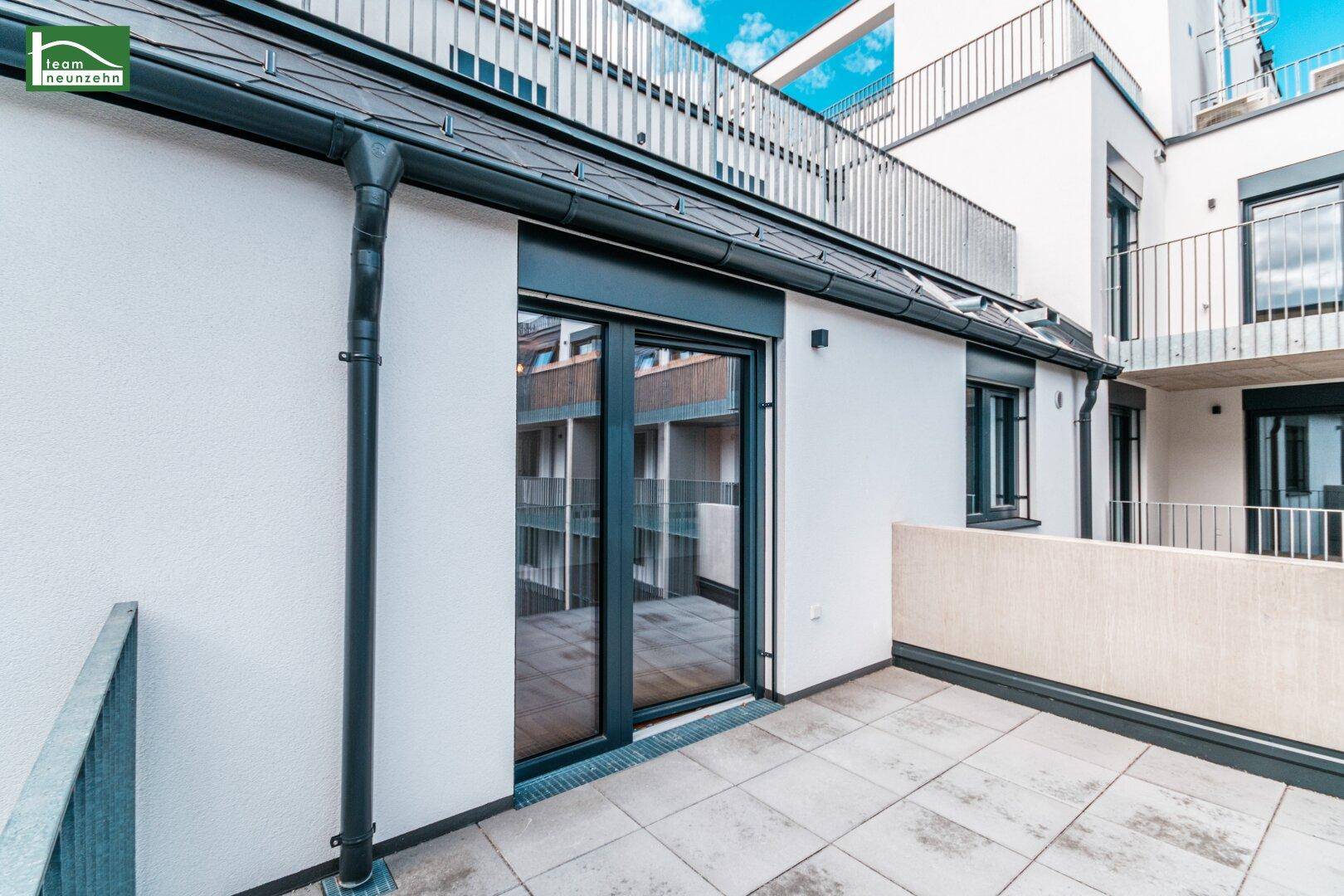 Moderne Terrasse mit Fliesenboden und Zugang zum Innenbereich durch große Glastüren.