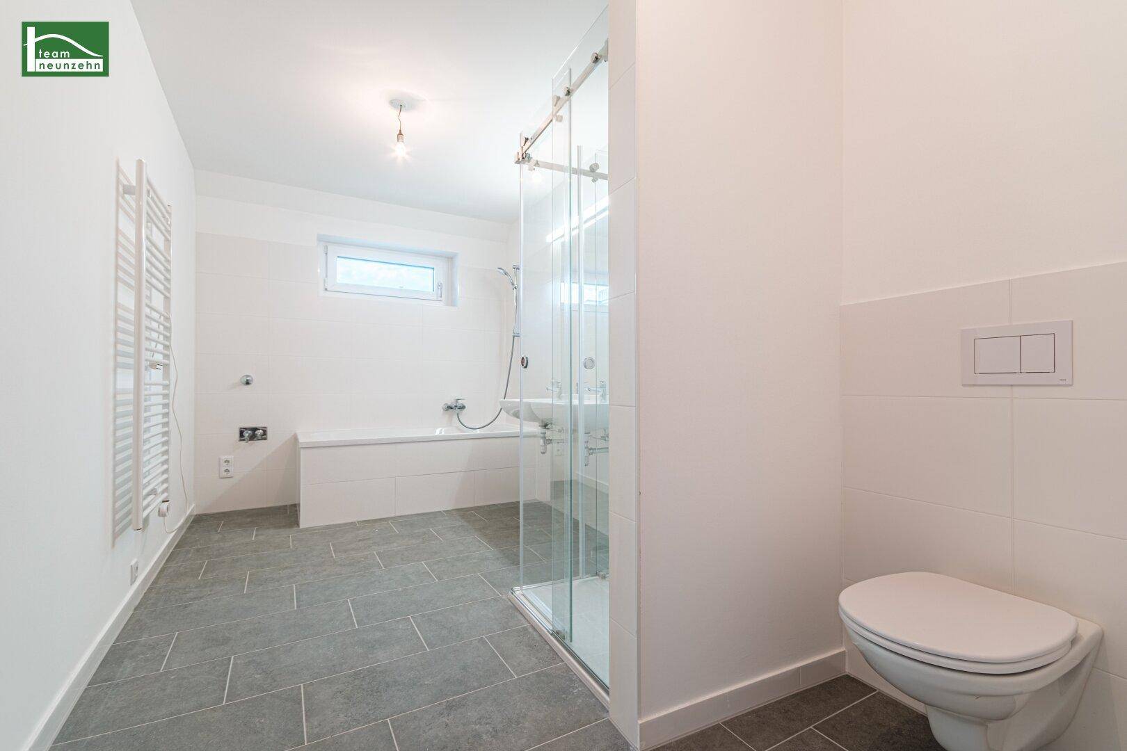 Modernes Badezimmer mit Badewanne, Dusche, WC und grauem Fliesenboden.