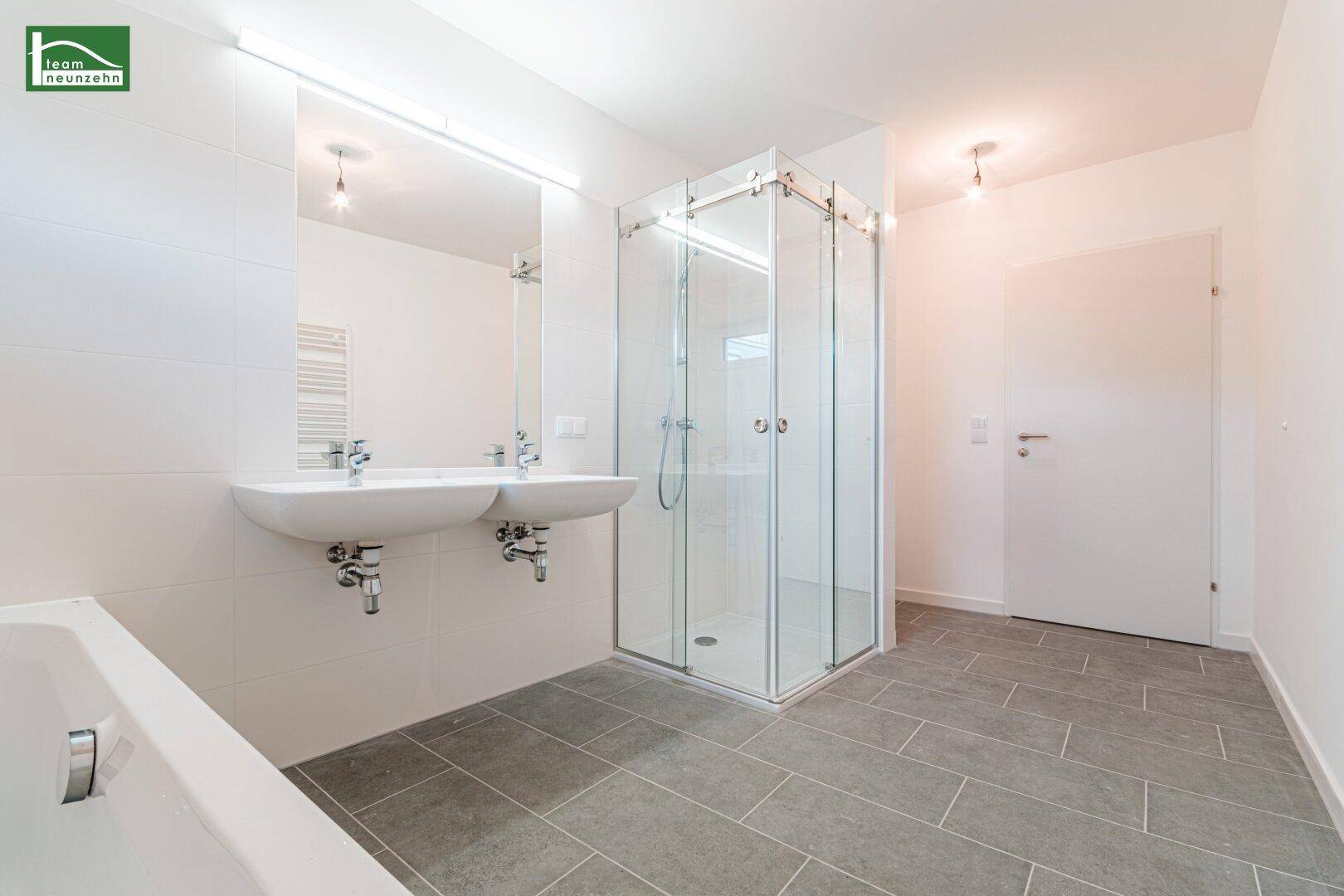 Helles Badezimmer mit Doppelwaschbecken, Duschkabine und Badewanne.