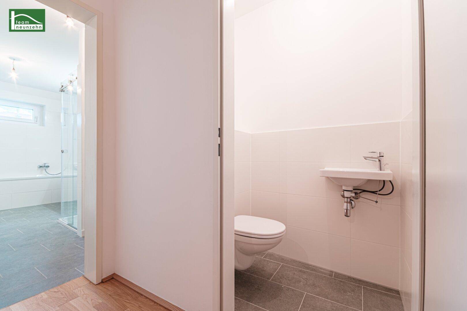 Separates Gäste-WC mit kleinem Waschbecken und Wand-WC, direkt neben dem Badezimmer.