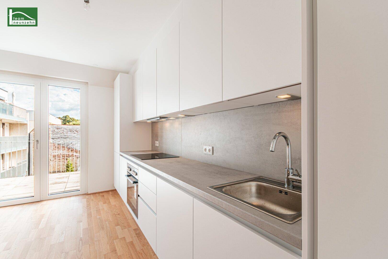 Moderne Einbauküche mit weißen Schränken, Spüle und Zugang zu einem Balkon.