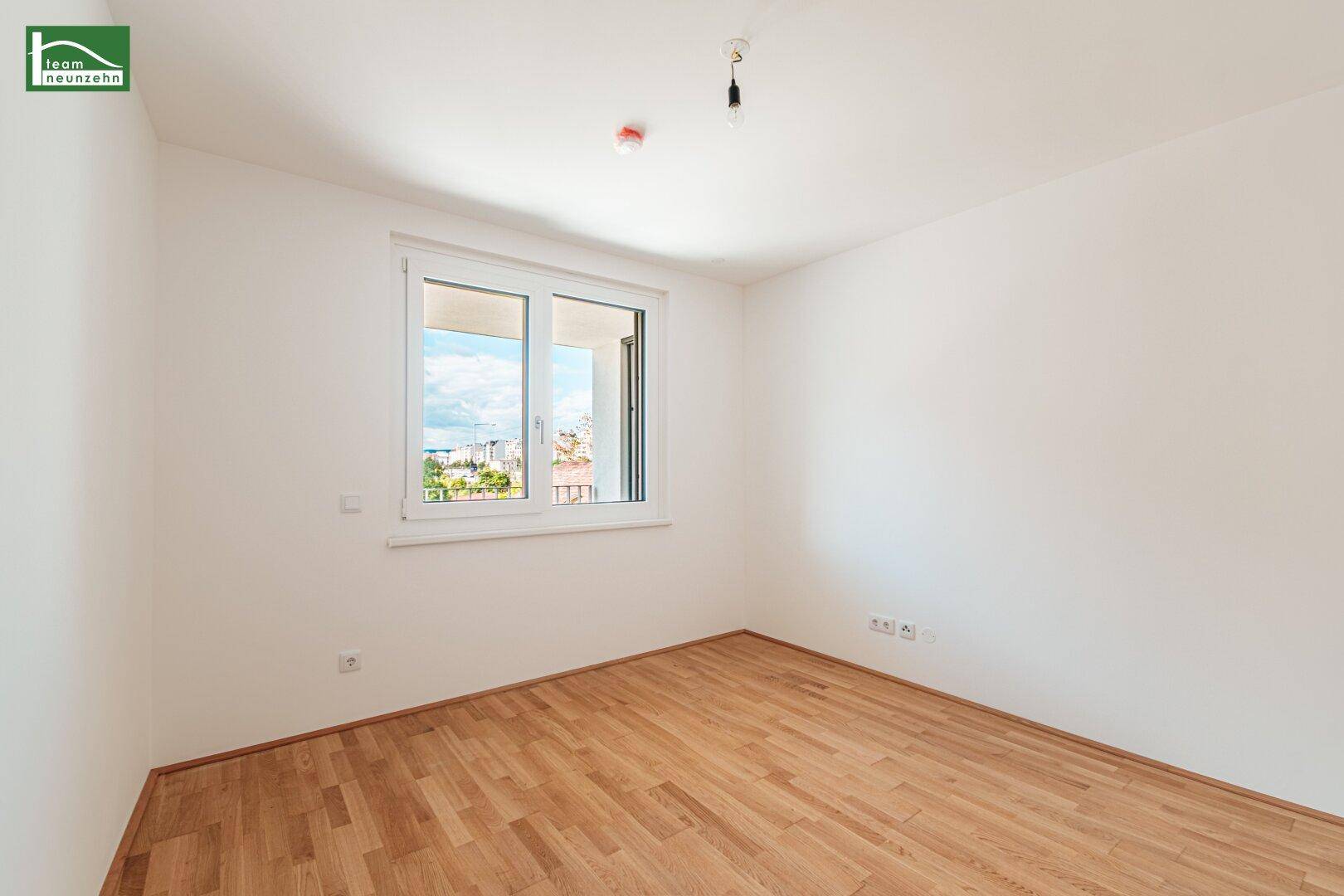 Heller Raum mit Parkettboden und Fenster, das einen Blick auf die Umgebung bietet.