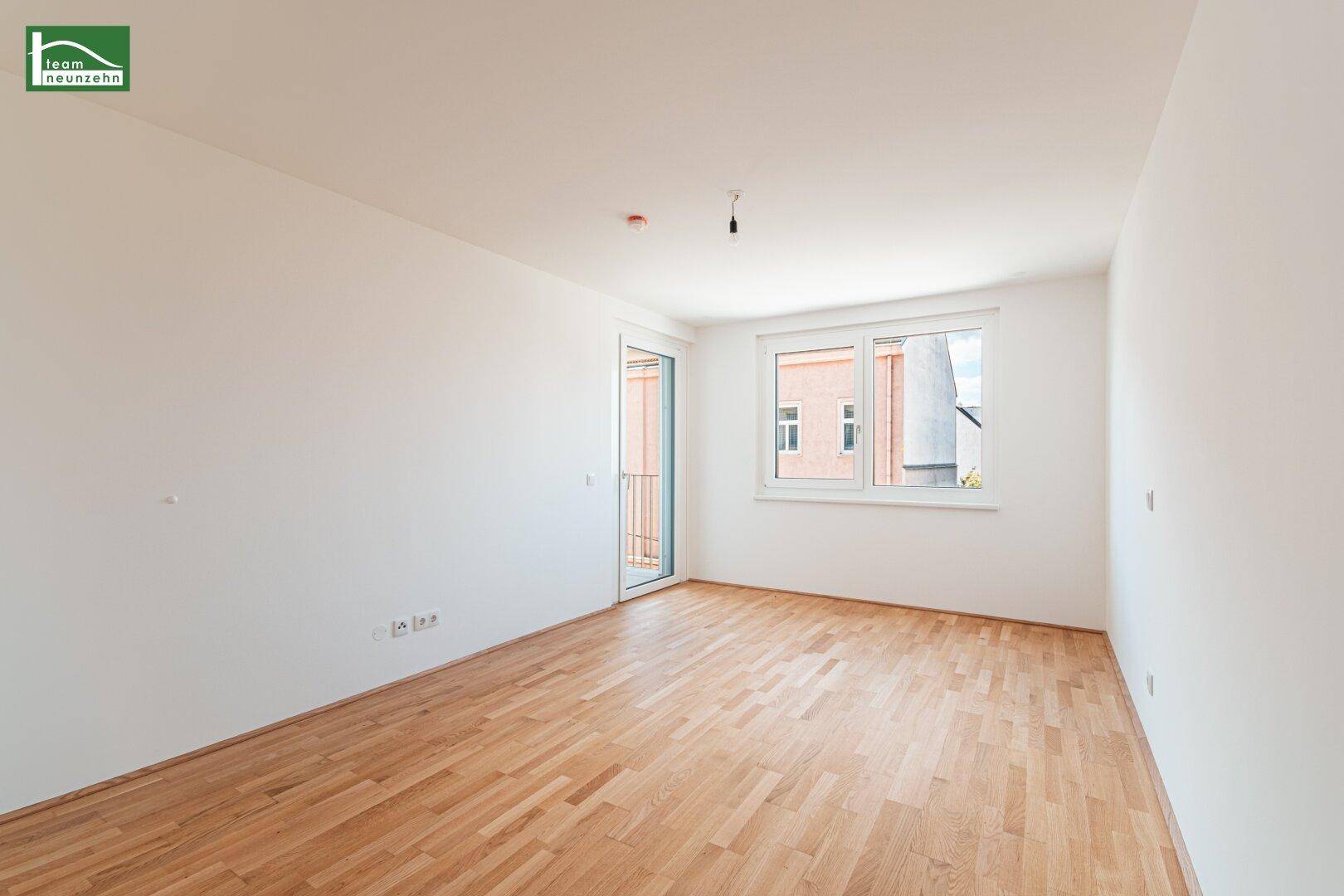 Heller Raum mit Parkettboden, Fenster und Zugang zu einem französischen Balkon.