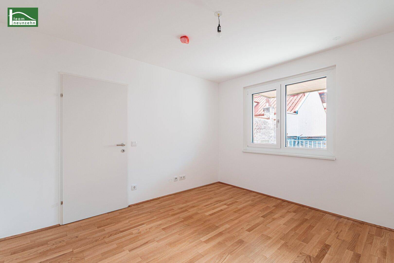 Unmöbliertes Schlafzimmer mit Parkettboden und einem Fenster, das Tageslicht hereinlässt.