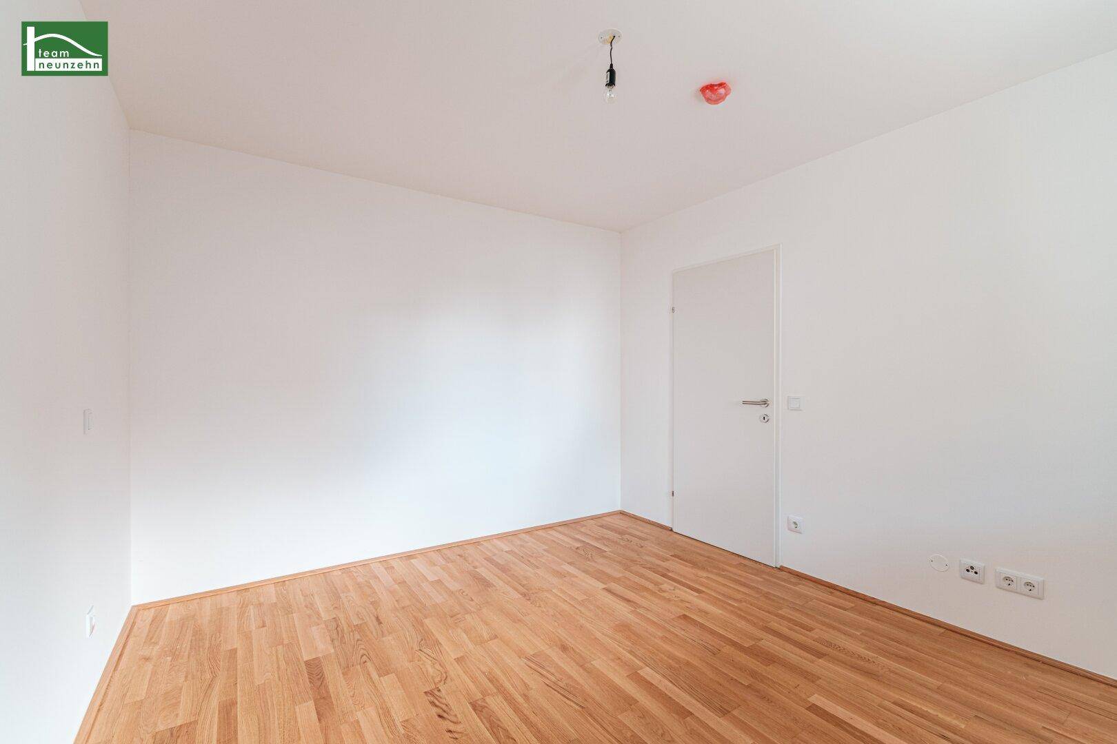 Leeres Zimmer mit hellem Parkettboden und weißen Wänden, ideal als Schlaf- oder Arbeitszimmer.