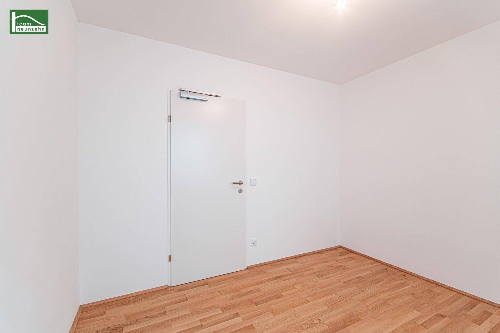 Unmöbliertes Zimmer mit Parkettboden und weißer Tür, bereit zur individuellen Gestaltung.