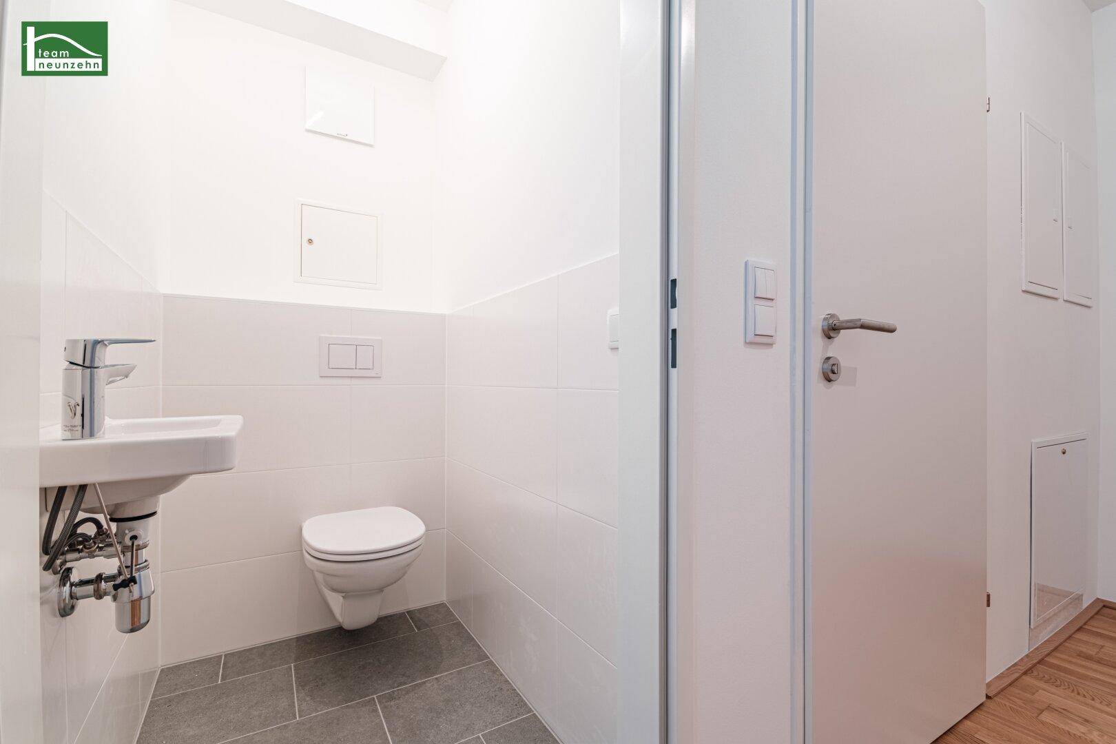 Separates WC mit wandhängender Toilette und kleinem Waschbecken, in modernem Design.