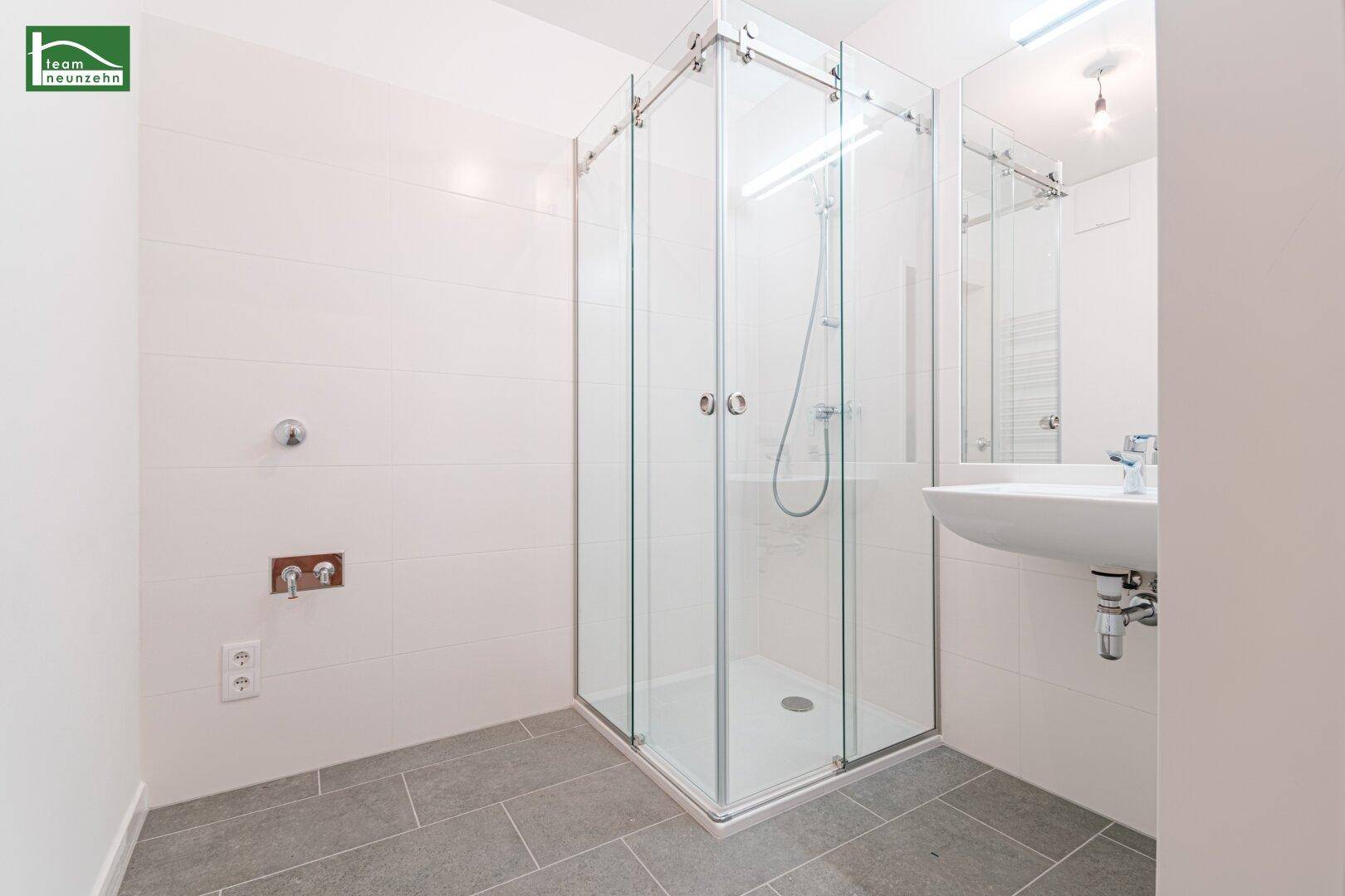 Modernes Badezimmer mit Duschkabine, Waschbecken und hellen Fliesen an Wänden und Boden.