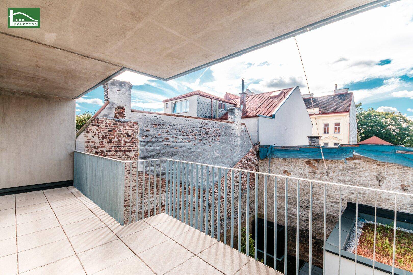 Geräumiger Balkon mit Fliesenboden und Blick auf die umliegenden Dächer und Gebäude.