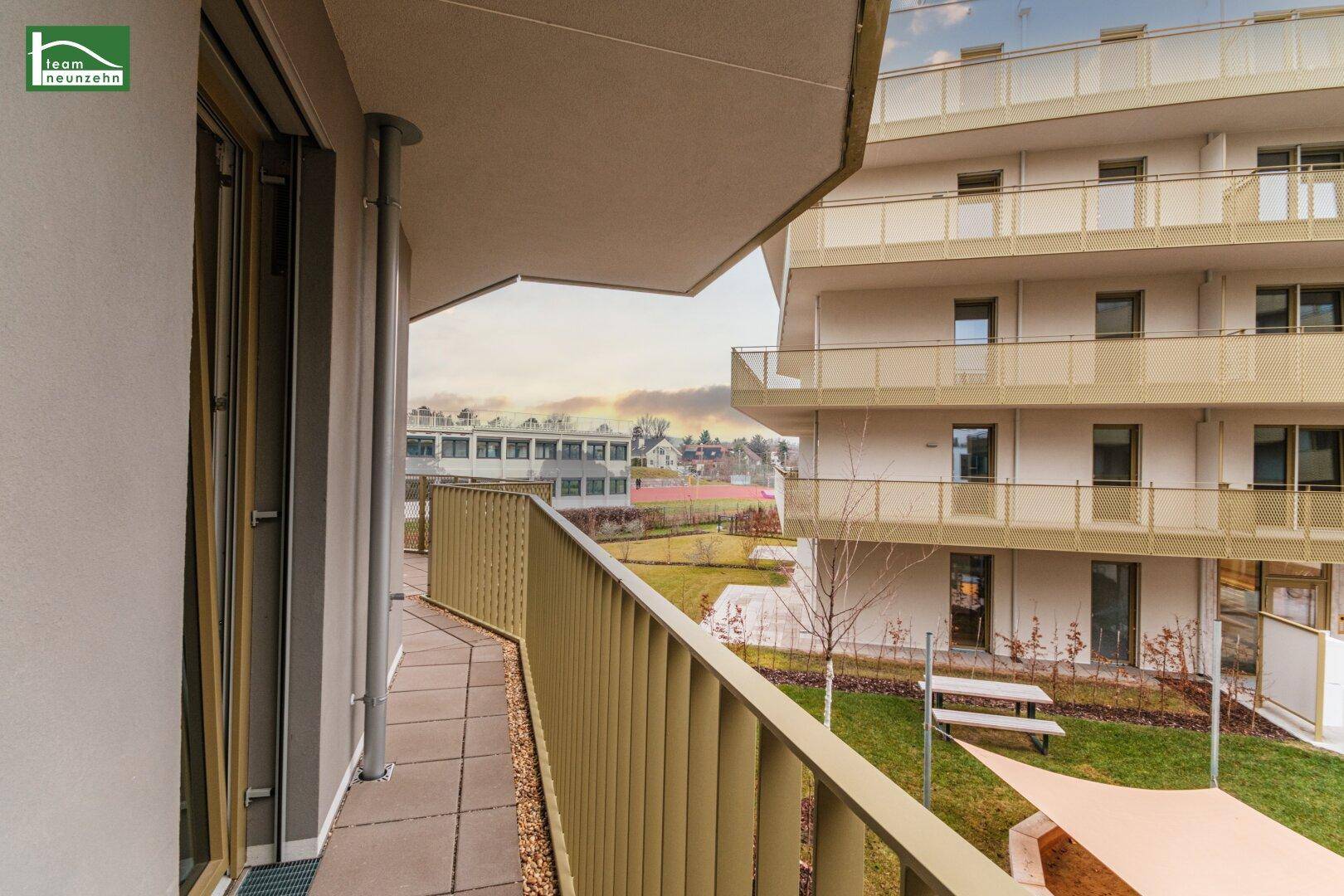 Heller Balkon mit Fliesenboden und Blick auf den begrünten Innenhof der Wohnanlage.