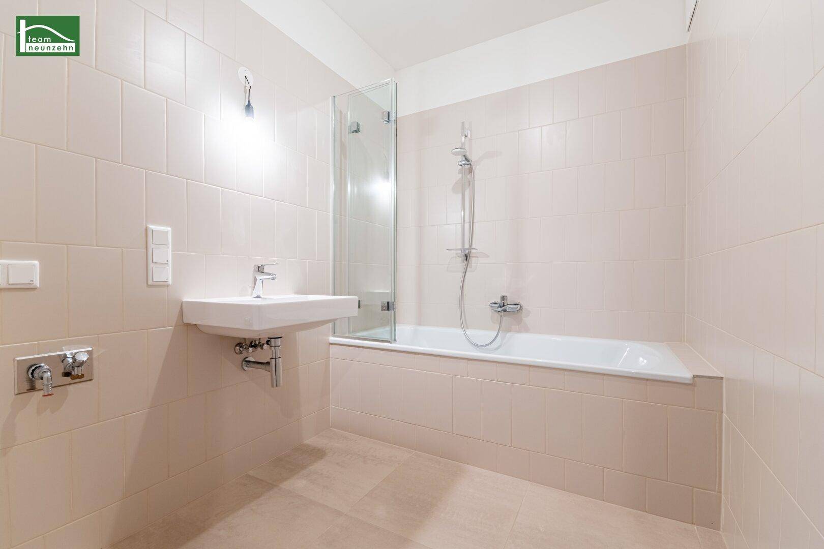 Modernes Badezimmer mit hellen Fliesen, Badewanne mit Duschwand und Einzelwaschbecken.