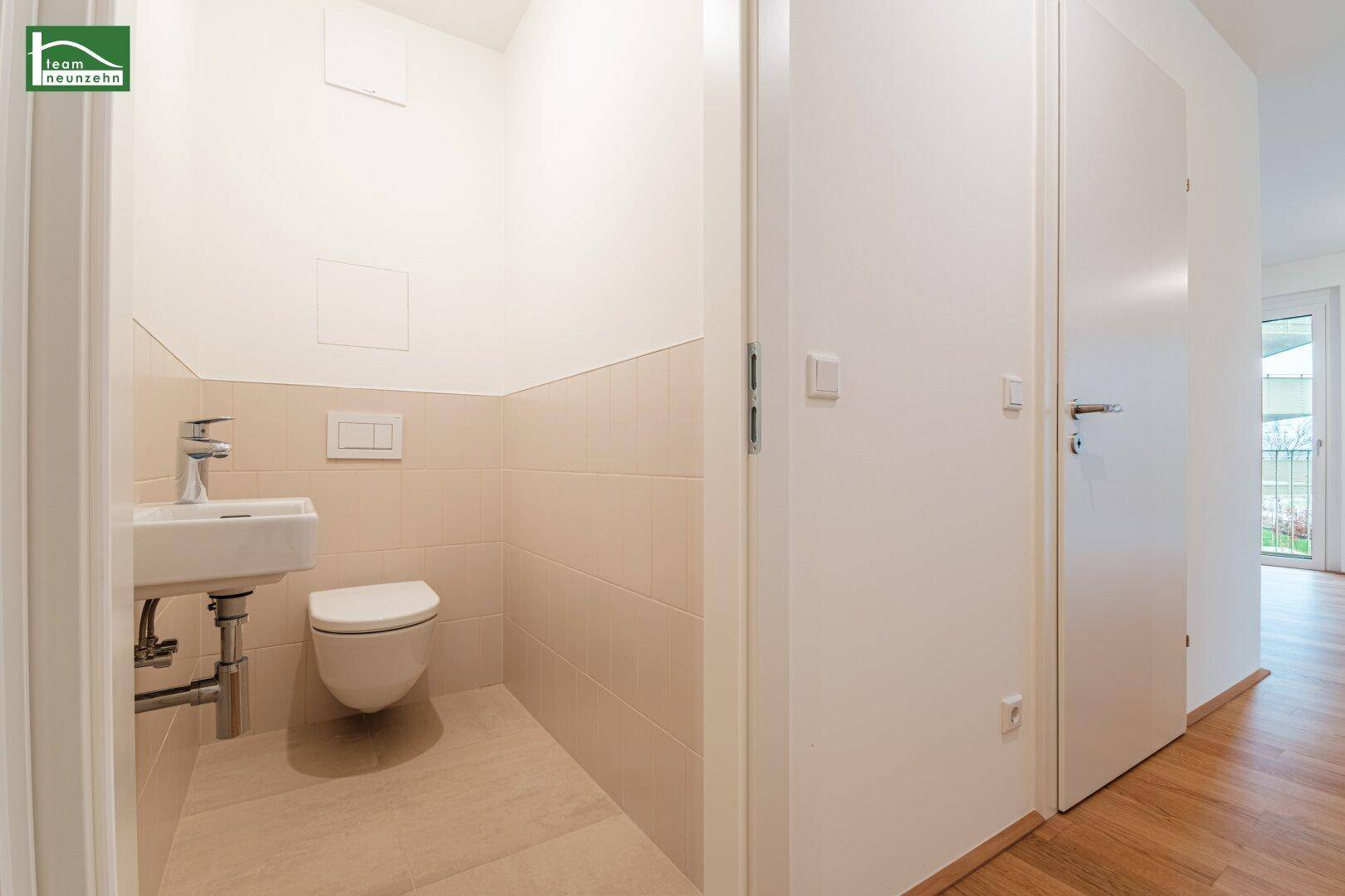 Gäste-WC mit wandhängender Toilette, kleinem Waschbecken und hellen Fliesen, sehr gepflegt.