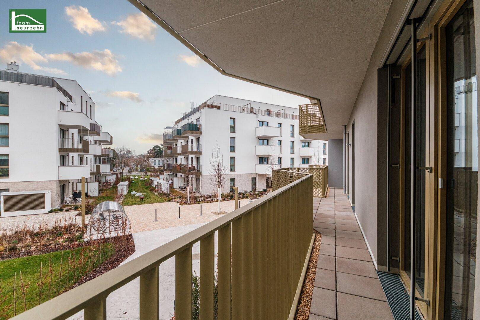 Langer Balkon mit Fliesenboden und Blick auf die moderne Wohnanlage, ideal für lange Abende.