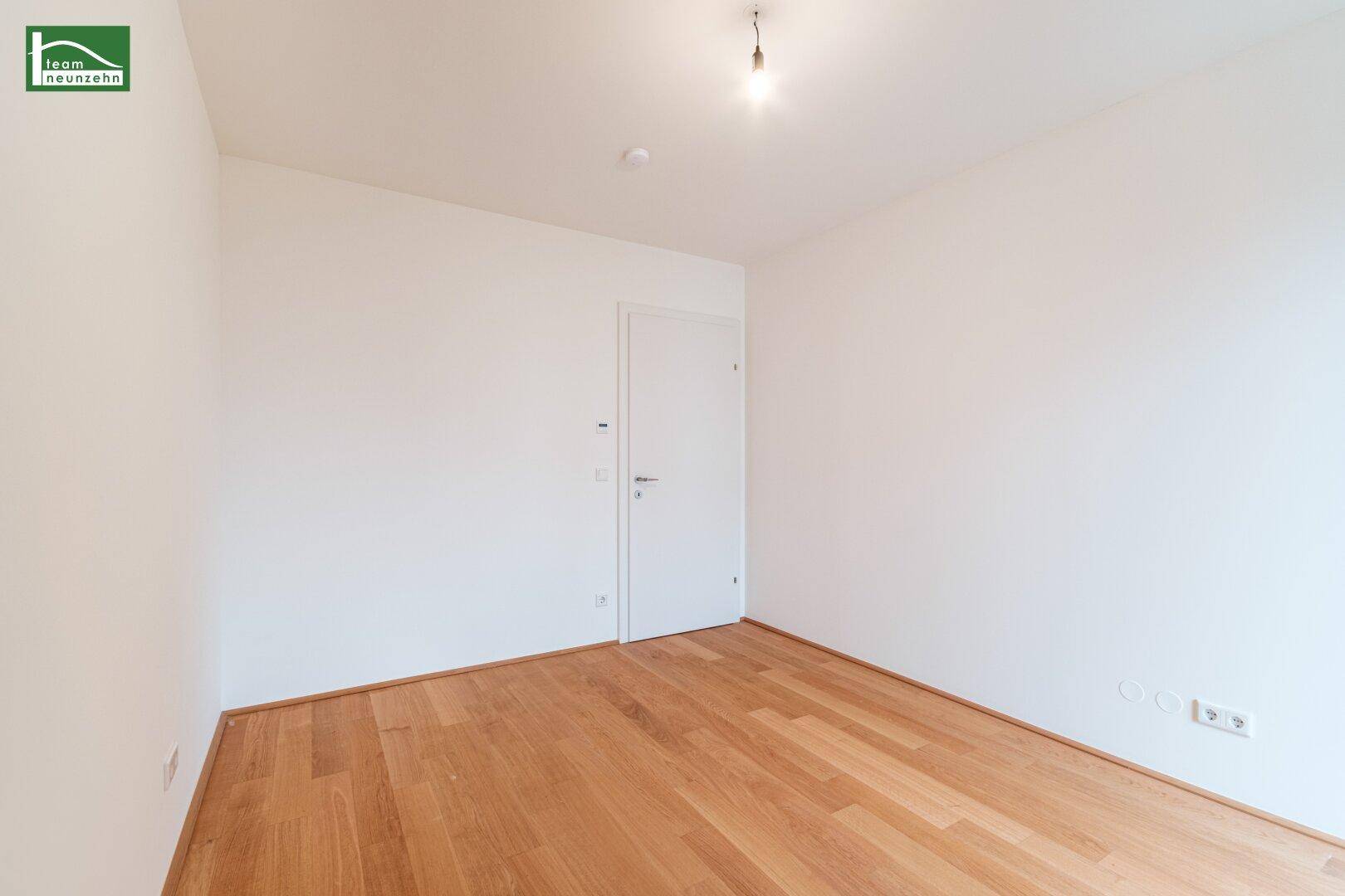 Leeres Zimmer mit Holzboden und weiß gestrichenen Wänden, ideal für ein Kinderzimmer.