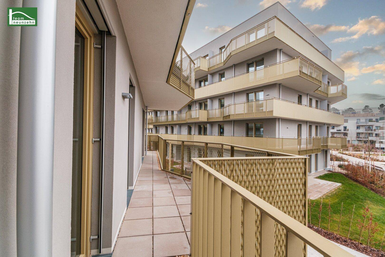 Langer Balkon mit Fliesenboden und Blick auf die moderne Wohnanlage.