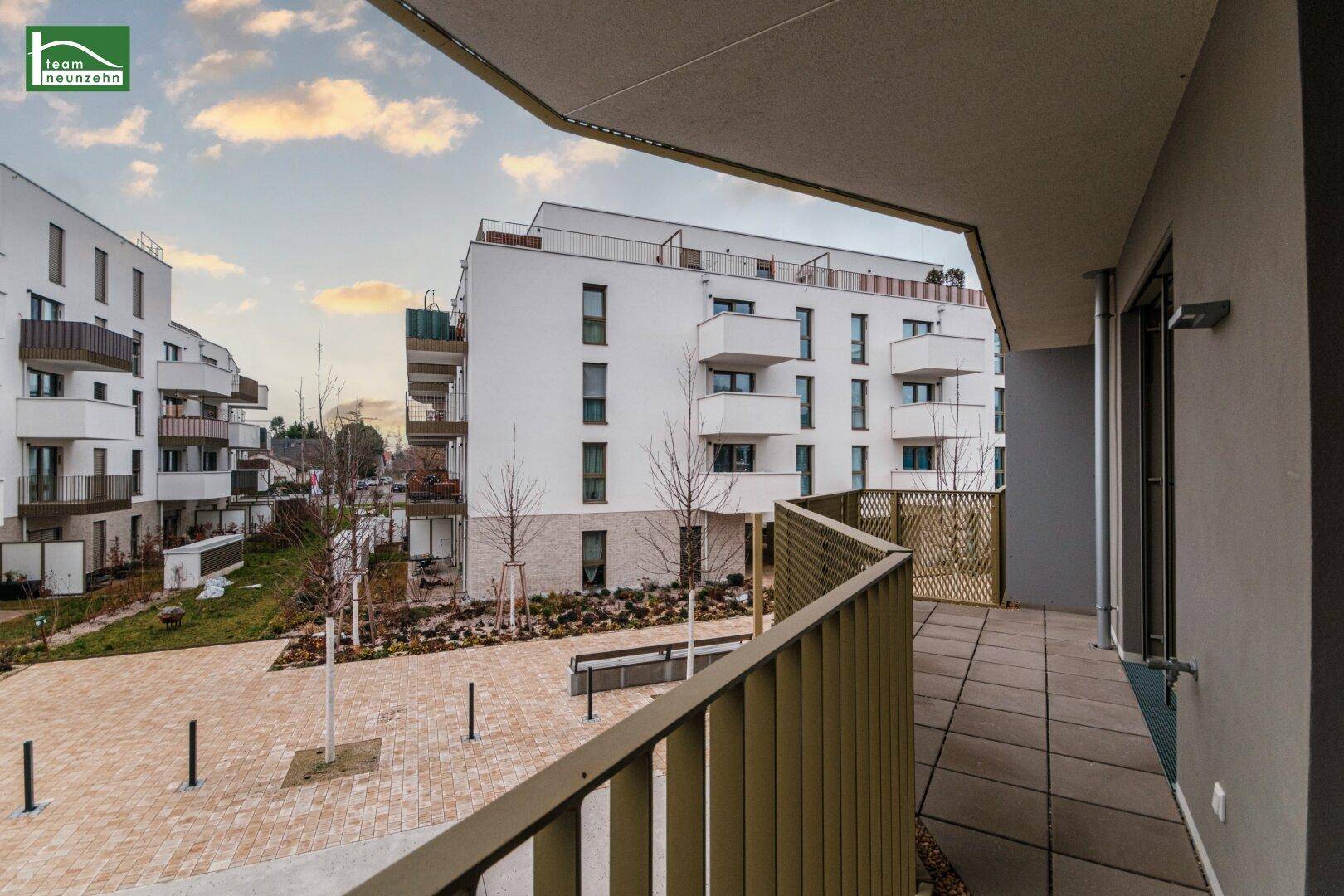 Langer Balkon mit Fliesenboden und weitem Blick über den begrünten Innenhof der Wohnanlage.
