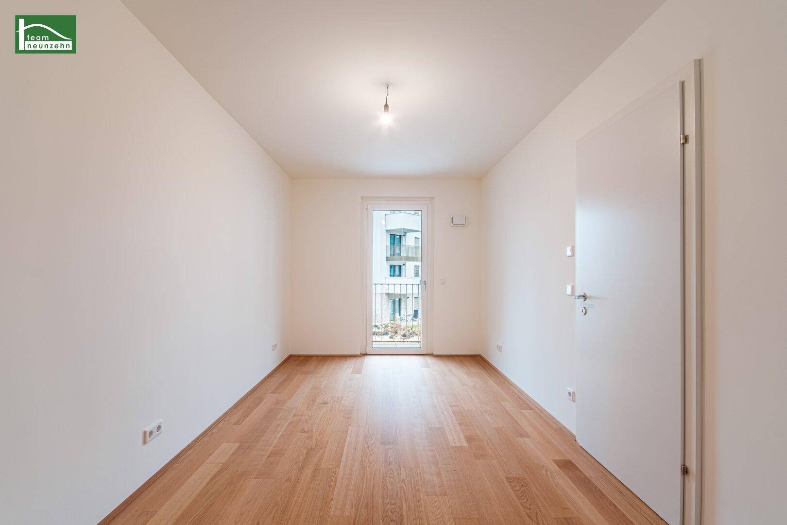 Leeres Zimmer mit Holzboden und Balkontür, ideal als Schlaf- oder Arbeitszimmer.
