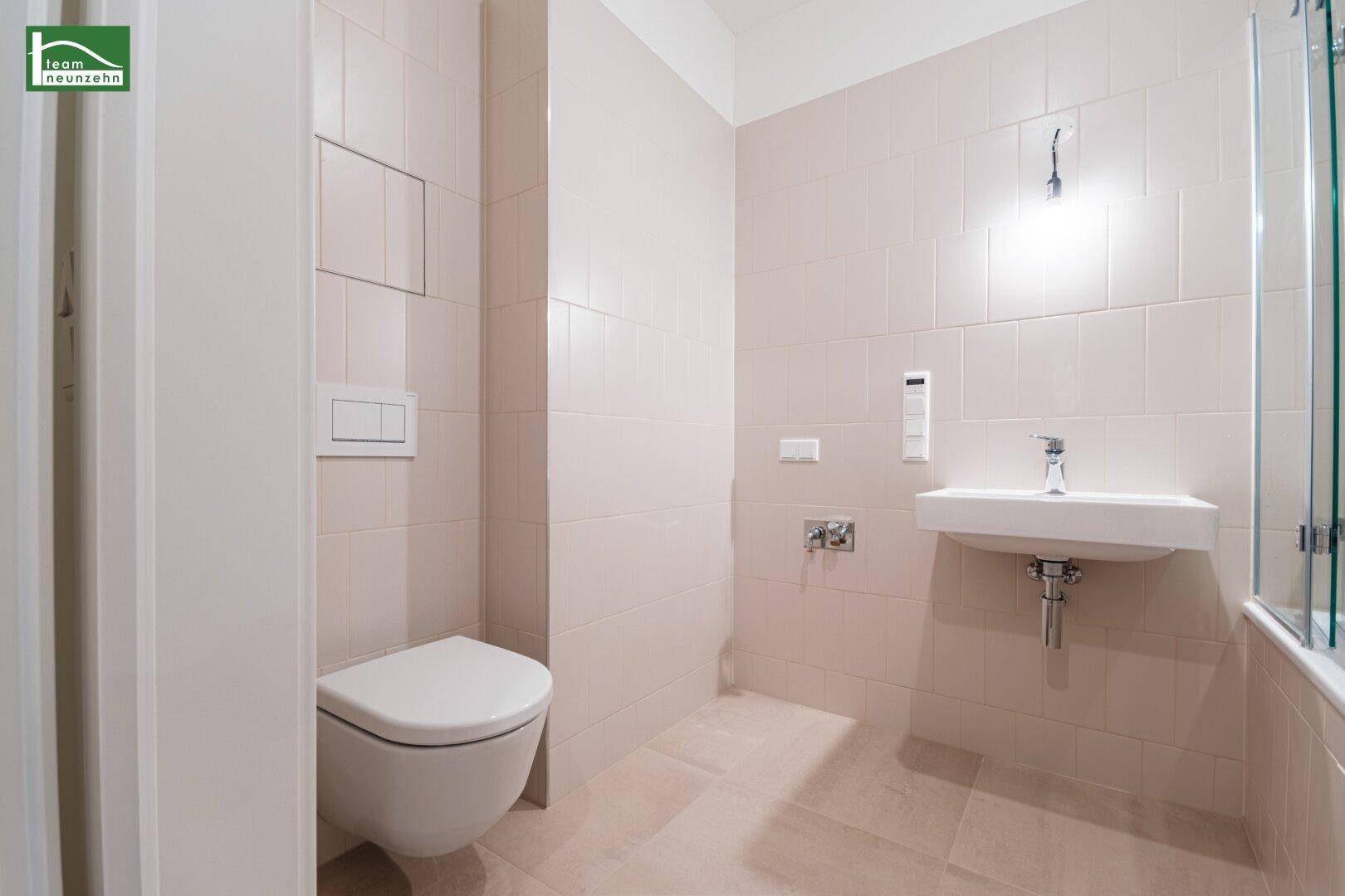 Separates WC mit wandhängender Toilette und kleinem Waschbecken, komplett gefliest.