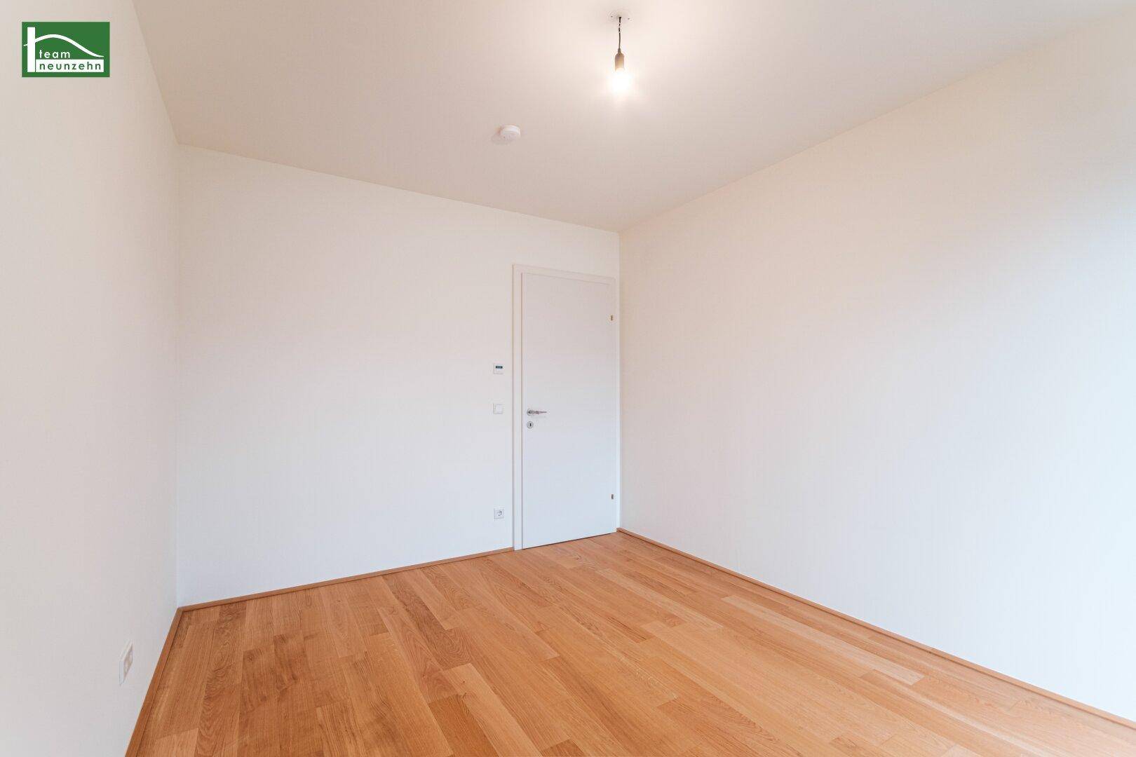Helles, leeres Zimmer mit Holzboden und weiß gestrichenen Wänden, vielseitig nutzbar.