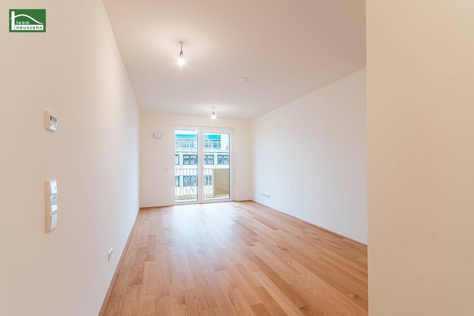 Helles, leeres Wohnzimmer mit Holzboden und Zugang zu einem Balkon, bereit zur individuellen Gestaltung.