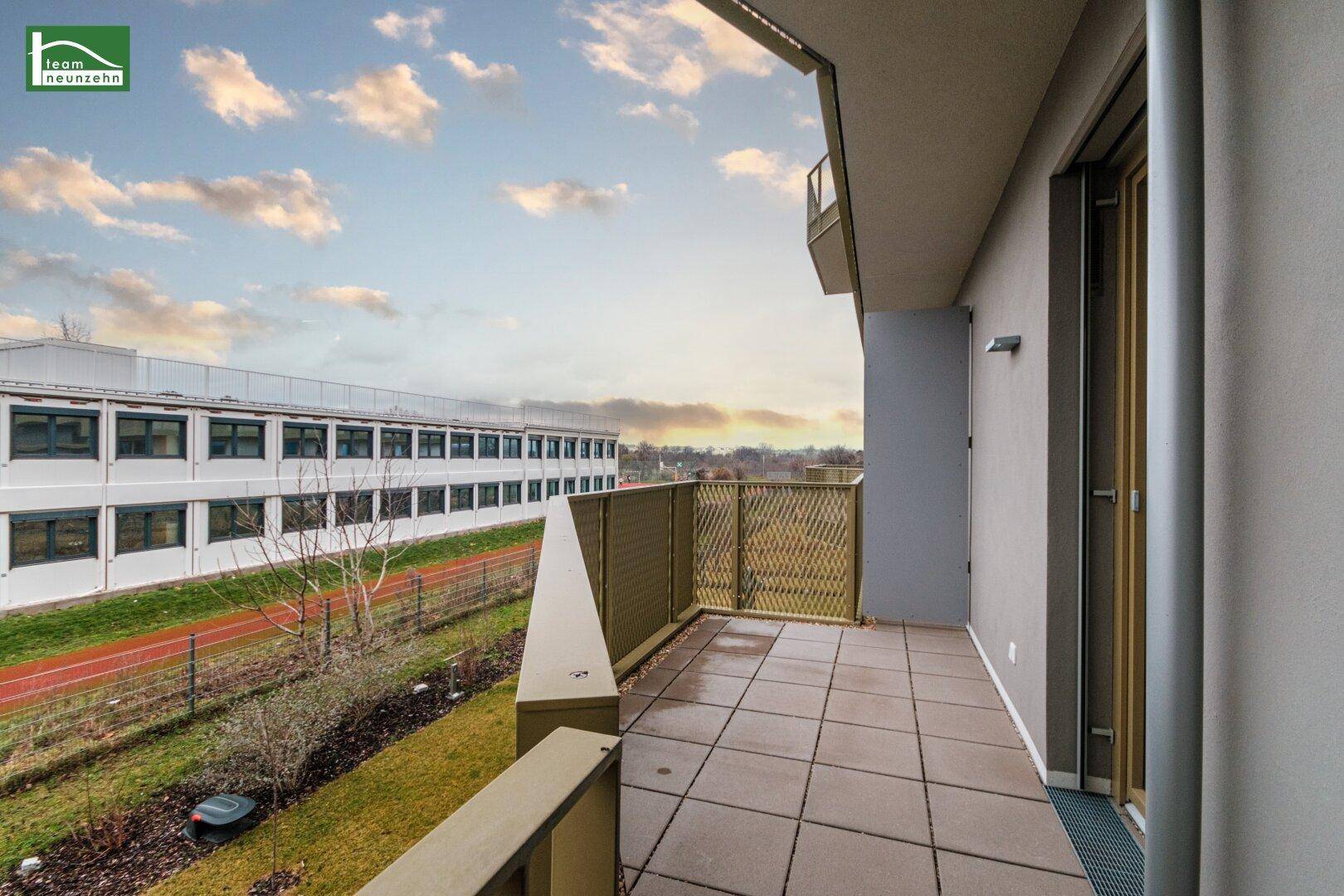Geräumiger Balkon mit Fliesenboden und Blick auf die umliegenden Gebäude und Grünflächen.