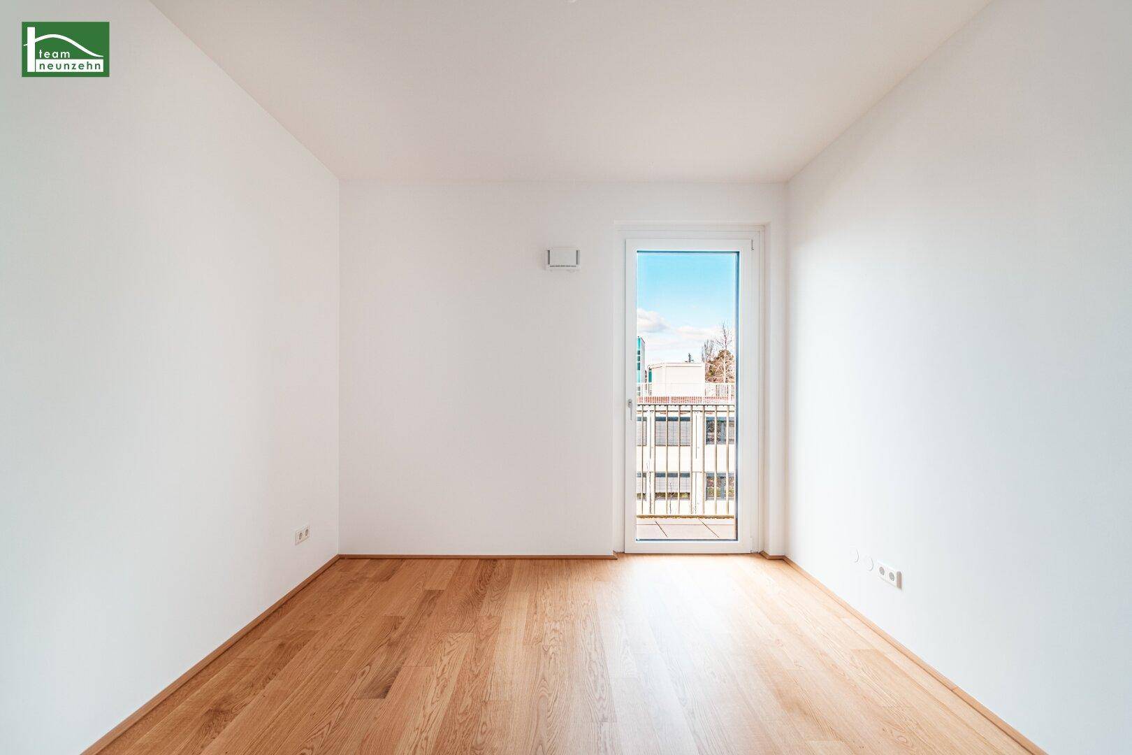 Helles, leeres Zimmer mit Holzboden und Zugang zu einem französischen Balkon.