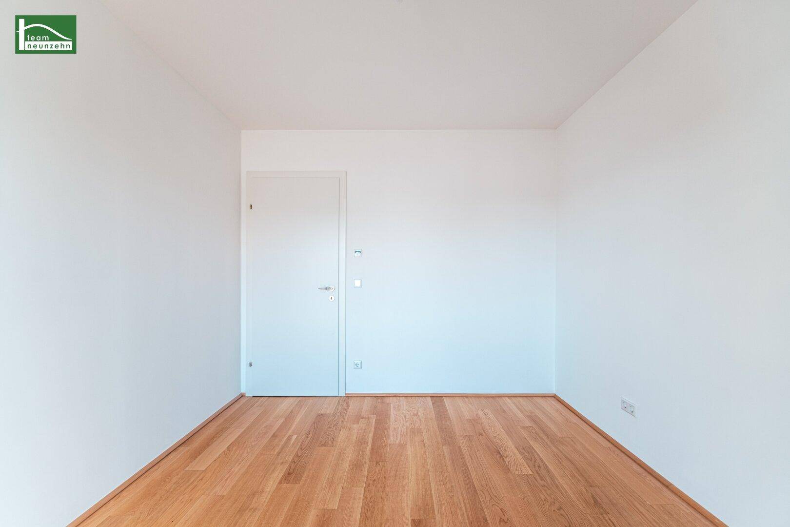 Leeres Zimmer mit Holzboden und weißer Tür, bereit für neue Einrichtungsideen in einem Neubau.