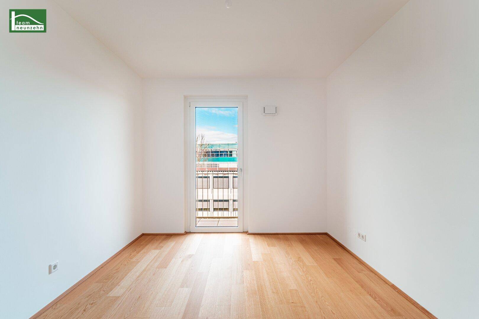 Helles, leeres Zimmer mit Eichenparkettboden und Zugang zu einem französischen Balkon.