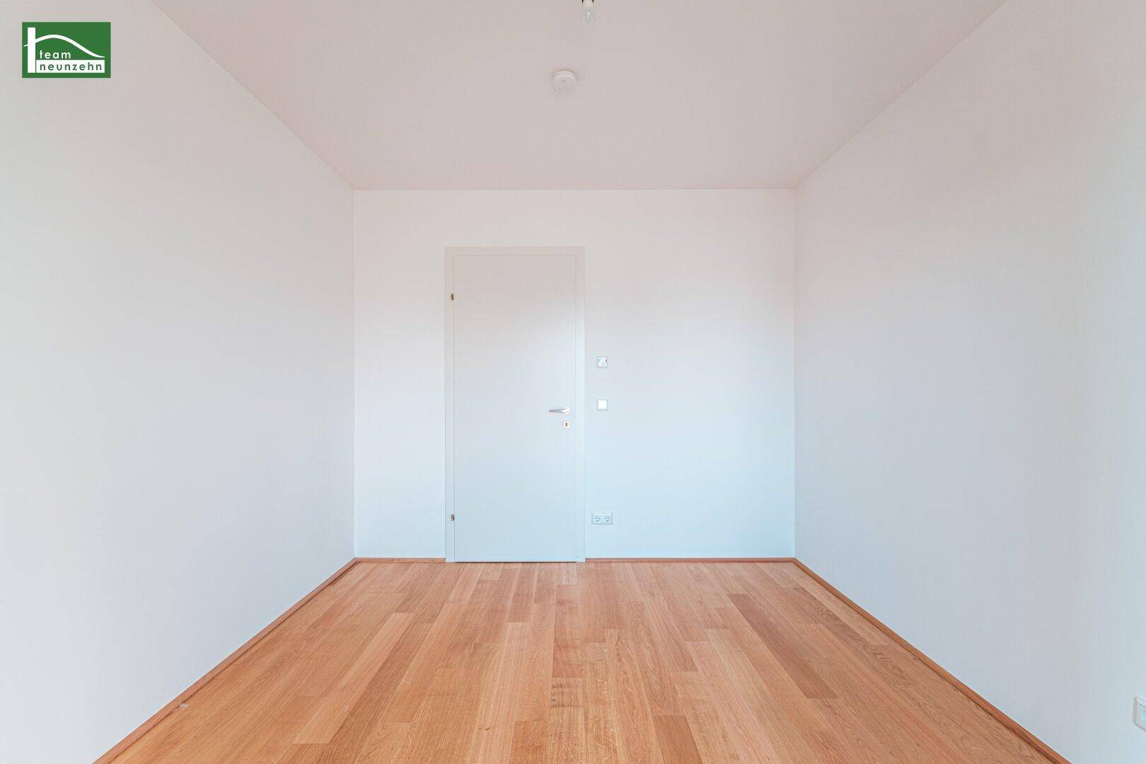 Leeres Zimmer mit Eichenparkettboden und weißer Tür, ideal als Kinder- oder Arbeitszimmer.