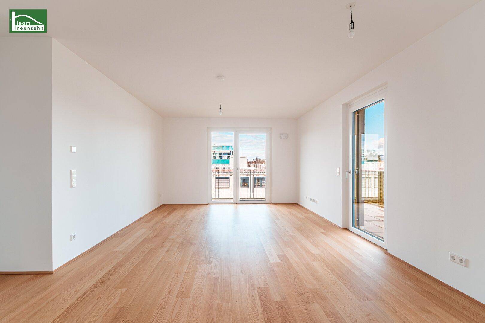 Helles, leeres Wohnzimmer mit Eichenparkettboden und Zugang zu einem Balkon.