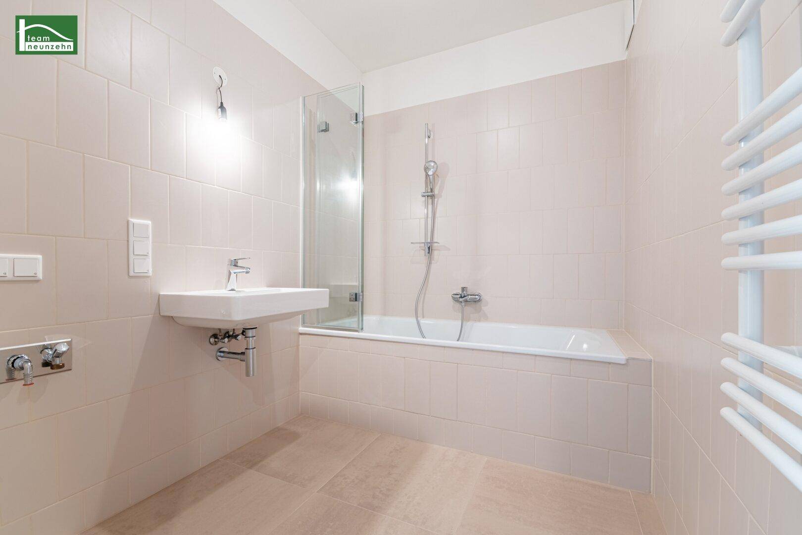 Modernes Badezimmer mit Badewanne, Duschabtrennung und beheiztem Handtuchhalter in hellen Fliesen.