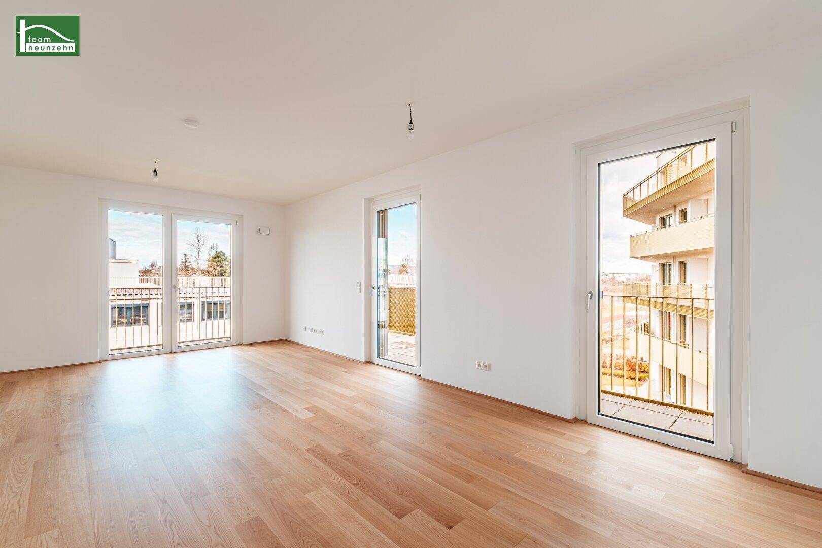 Geräumiges, leeres Wohnzimmer mit hellem Parkettboden und mehreren Balkonzugängen.