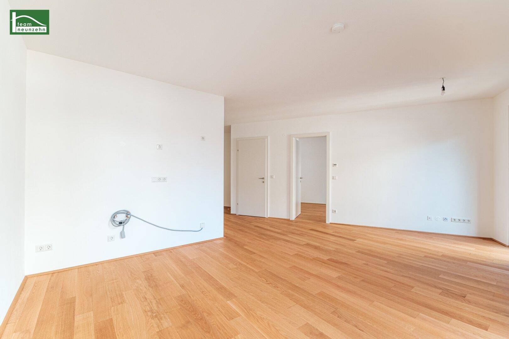 Geräumiges, leeres Wohnzimmer mit hellem Parkettboden und weißen Wänden.
