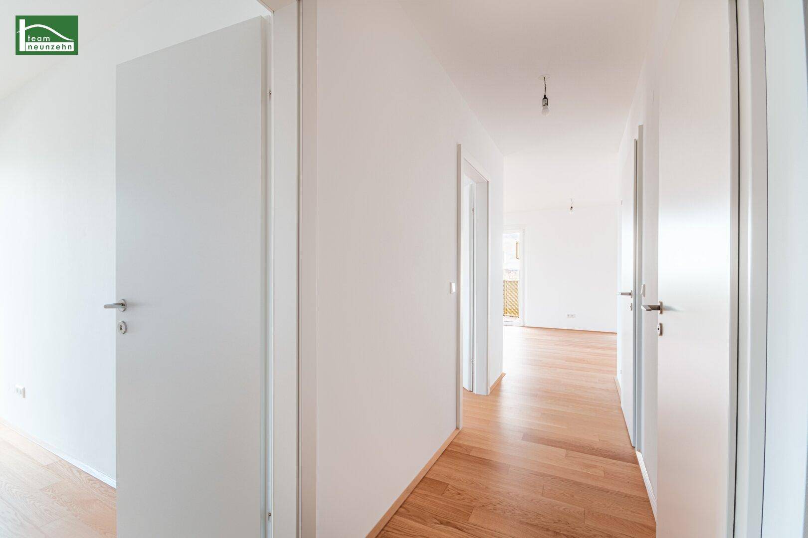 Heller Flur mit Holzboden und mehreren Türen zu den angrenzenden Räumen in einem Neubau.