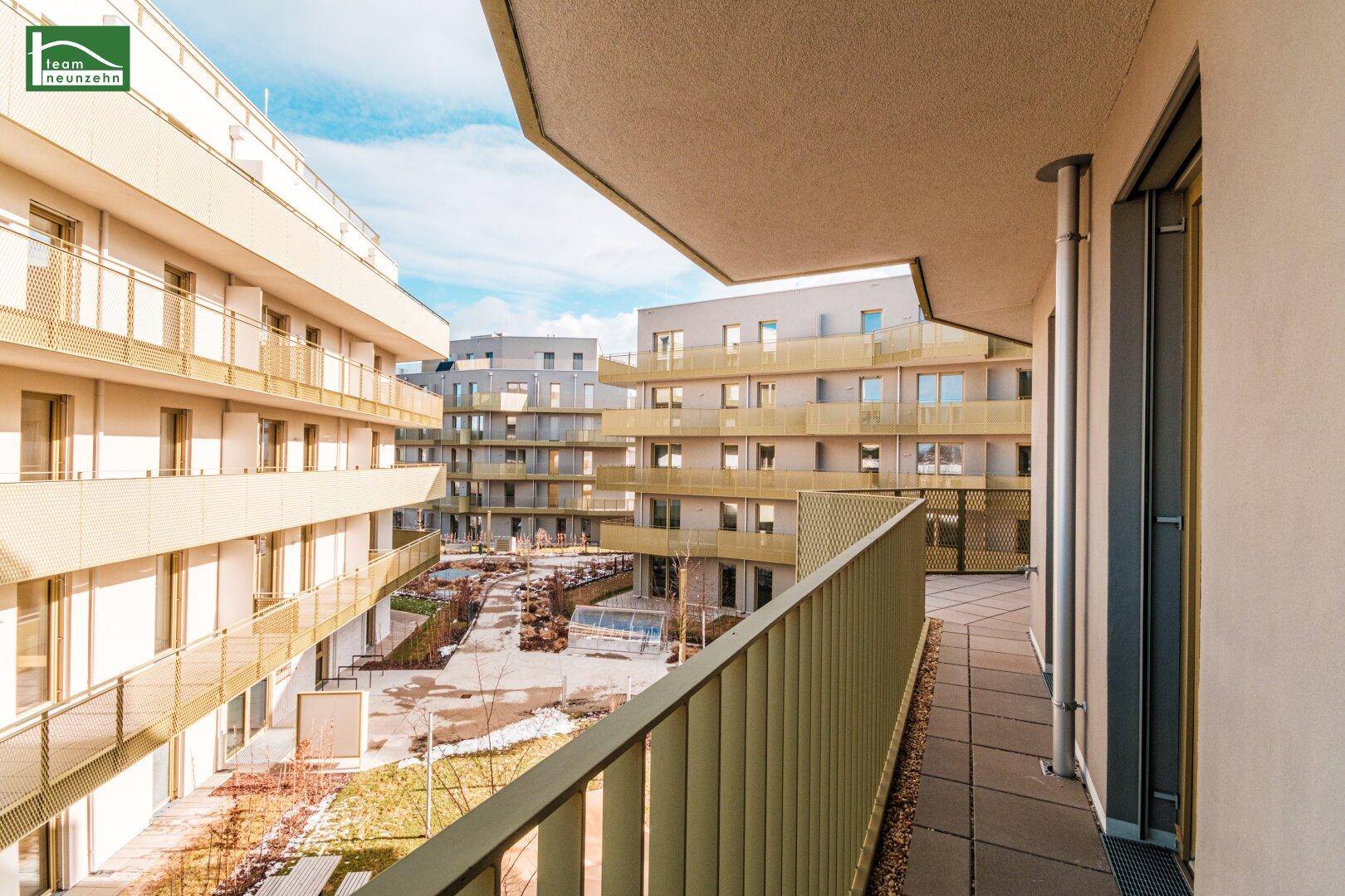 Geräumiger Balkon mit Fliesenboden und Blick auf den begrünten Innenhof der Wohnanlage.