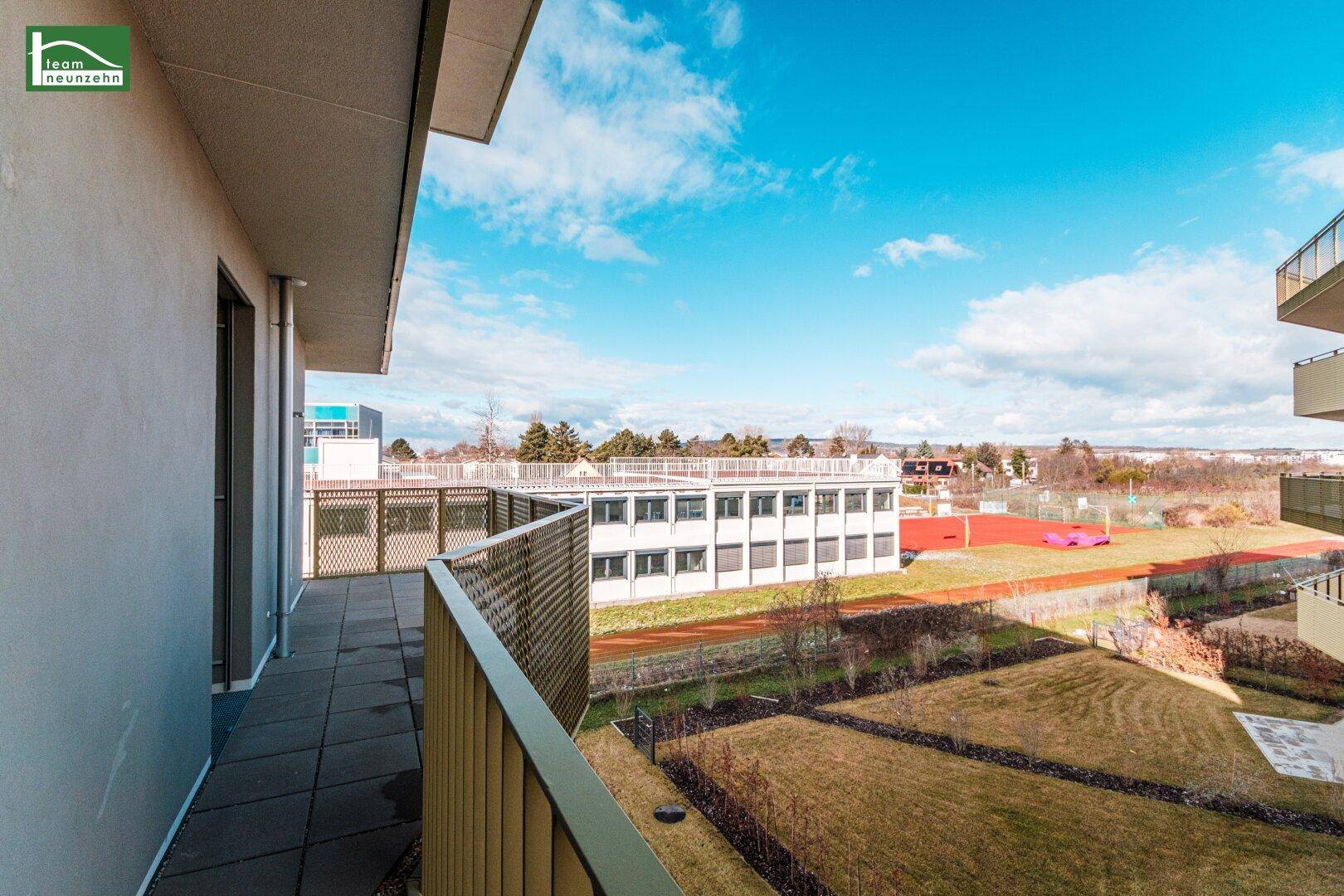 Langer Balkon mit Blick auf die grüne Umgebung und ein Sportfeld.