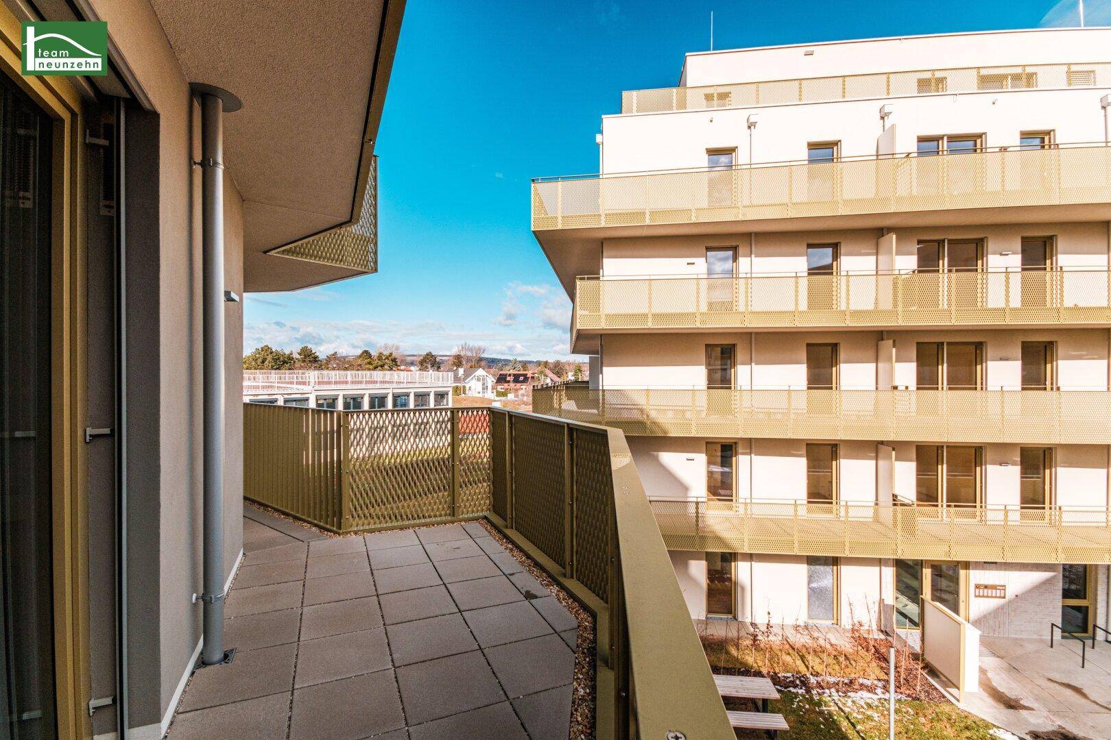 Heller Balkon mit Fliesenboden und Blick auf die umliegenden Gebäude und die grüne Umgebung.