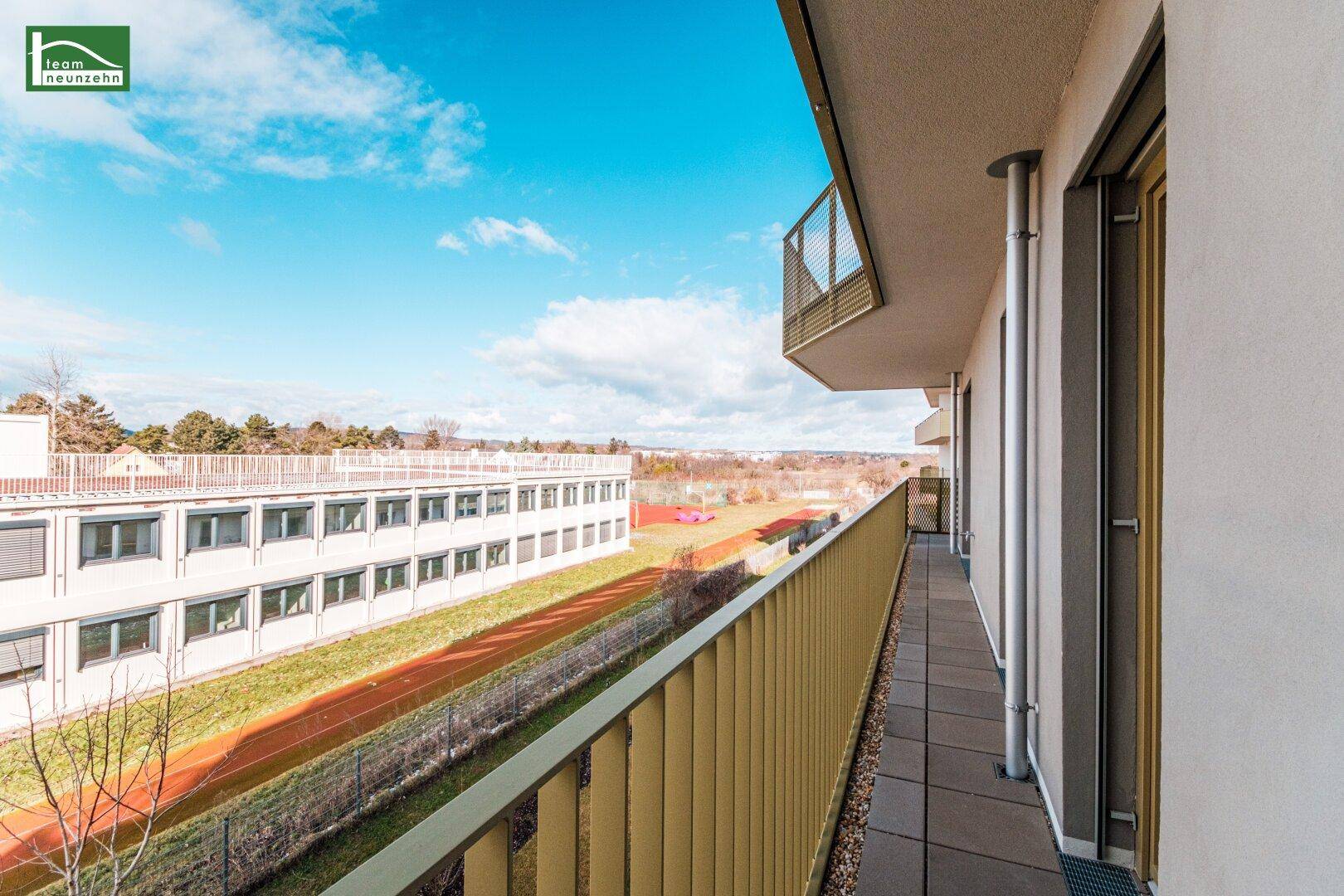 Breiter Balkon mit Blick auf die grüne Umgebung und weitere Gebäude.