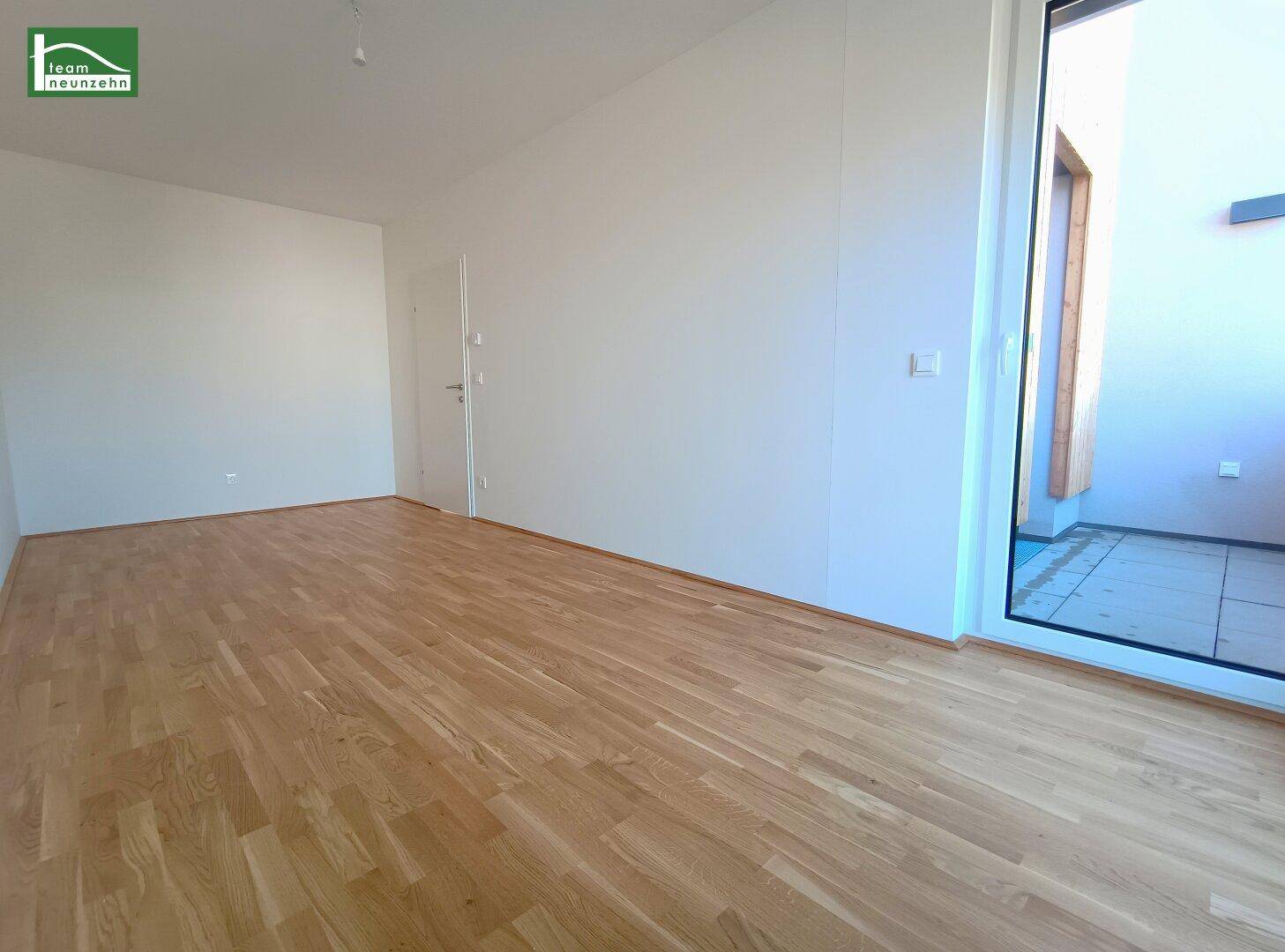 Leeres Zimmer mit Parkettboden und Zugang zu einem kleinen Balkon.