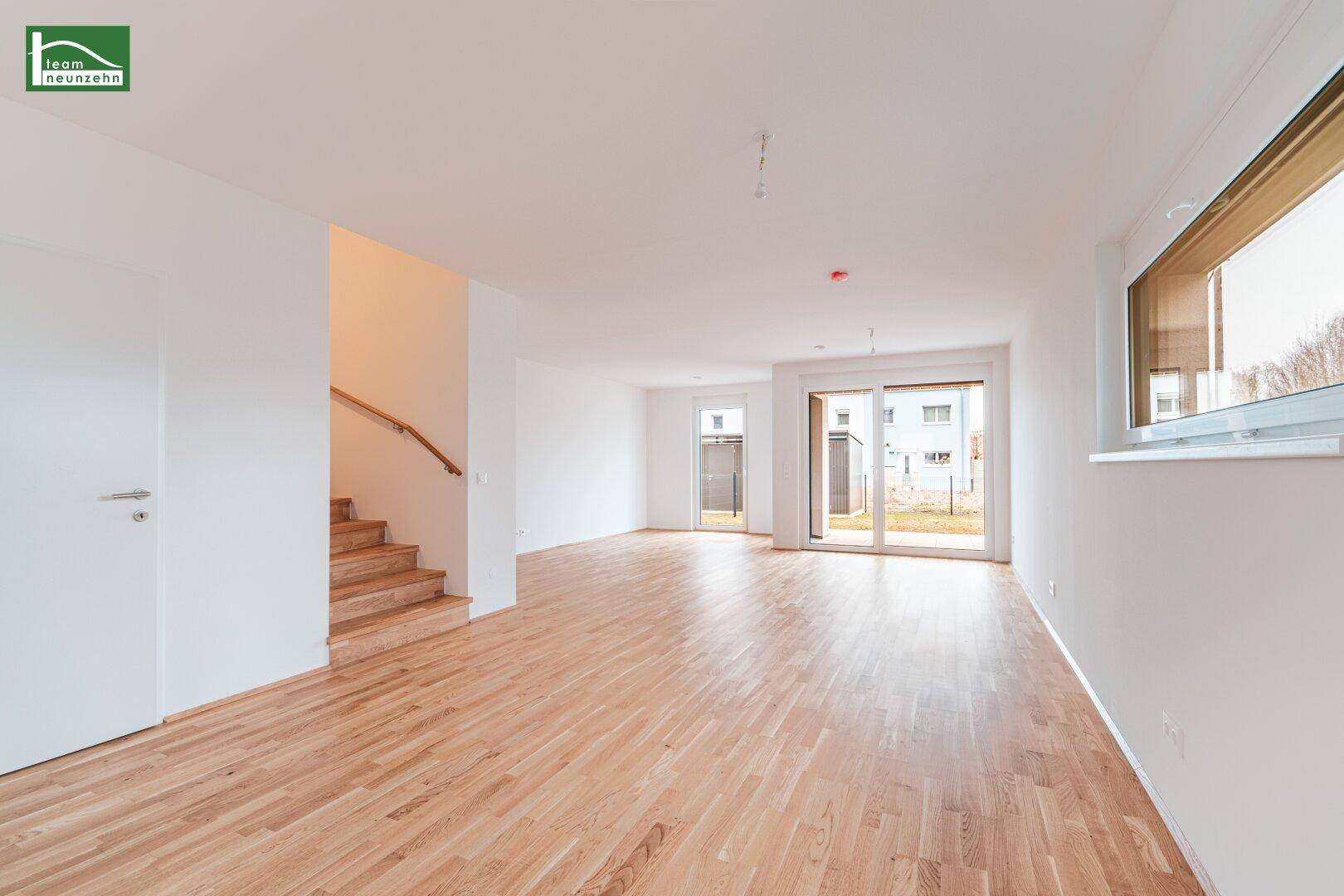 Helles, leeres Wohnzimmer mit Holzparkettboden und Zugang zur Terrasse.