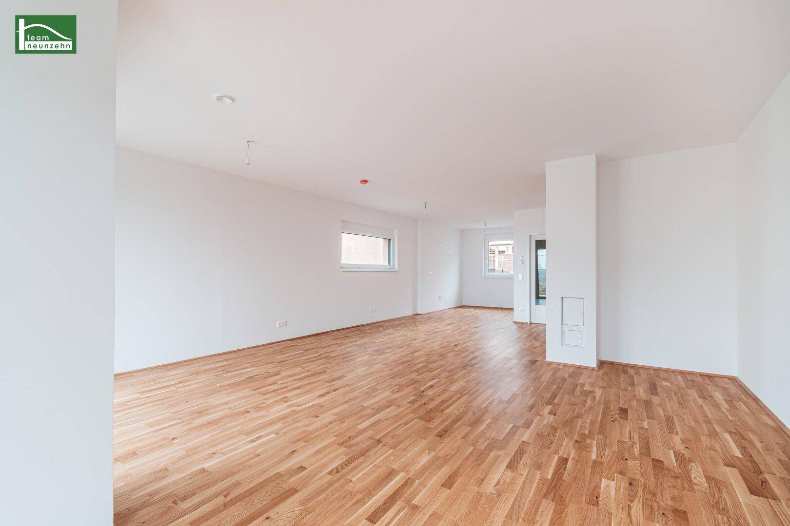 Geräumiges, leeres Wohnzimmer mit hellem Parkettboden und viel Tageslicht.