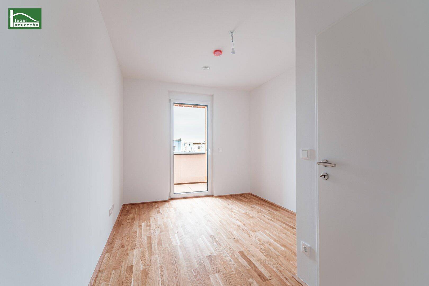 Helles Schlafzimmer mit Parkettboden und Zugang zu einem französischen Balkon.