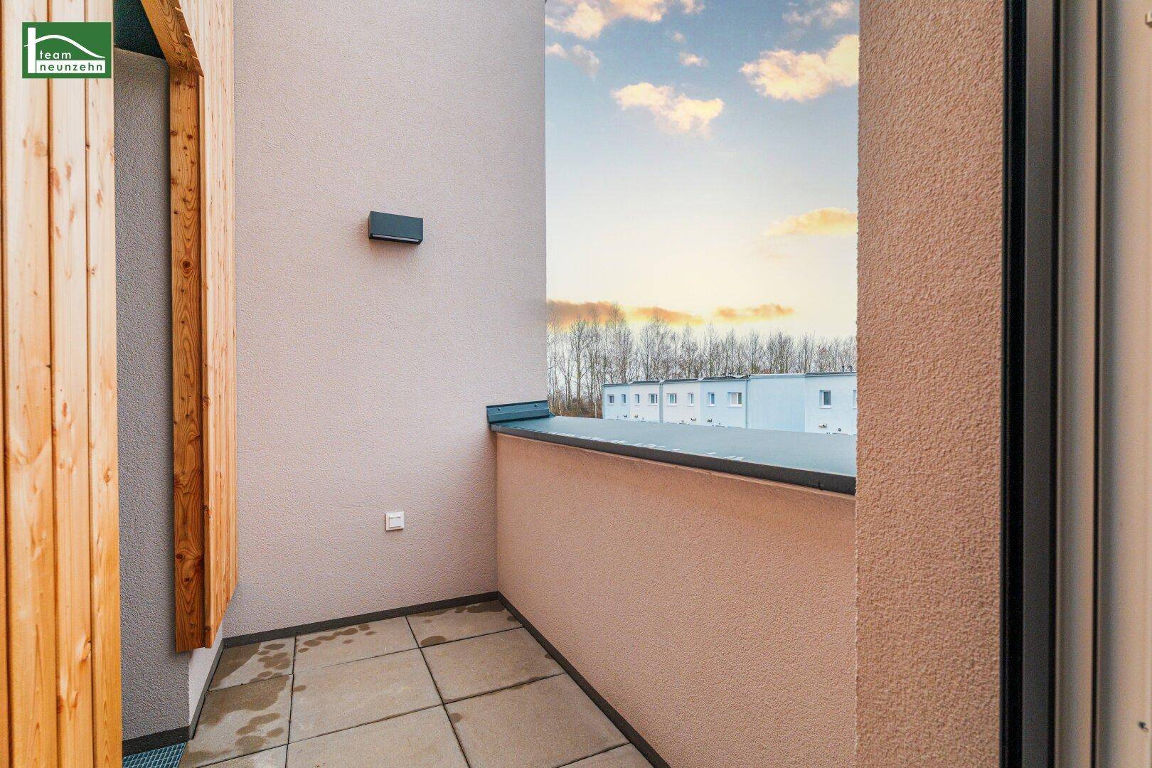Kleiner Balkon mit Fliesenboden und Blick auf die Umgebung unter blauem Himmel.