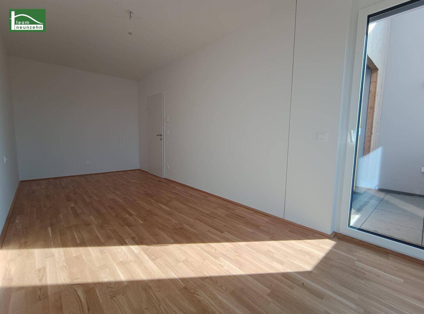 Schlafzimmer mit Parkettboden und Balkonzugang, durchflutet von Sonnenlicht.